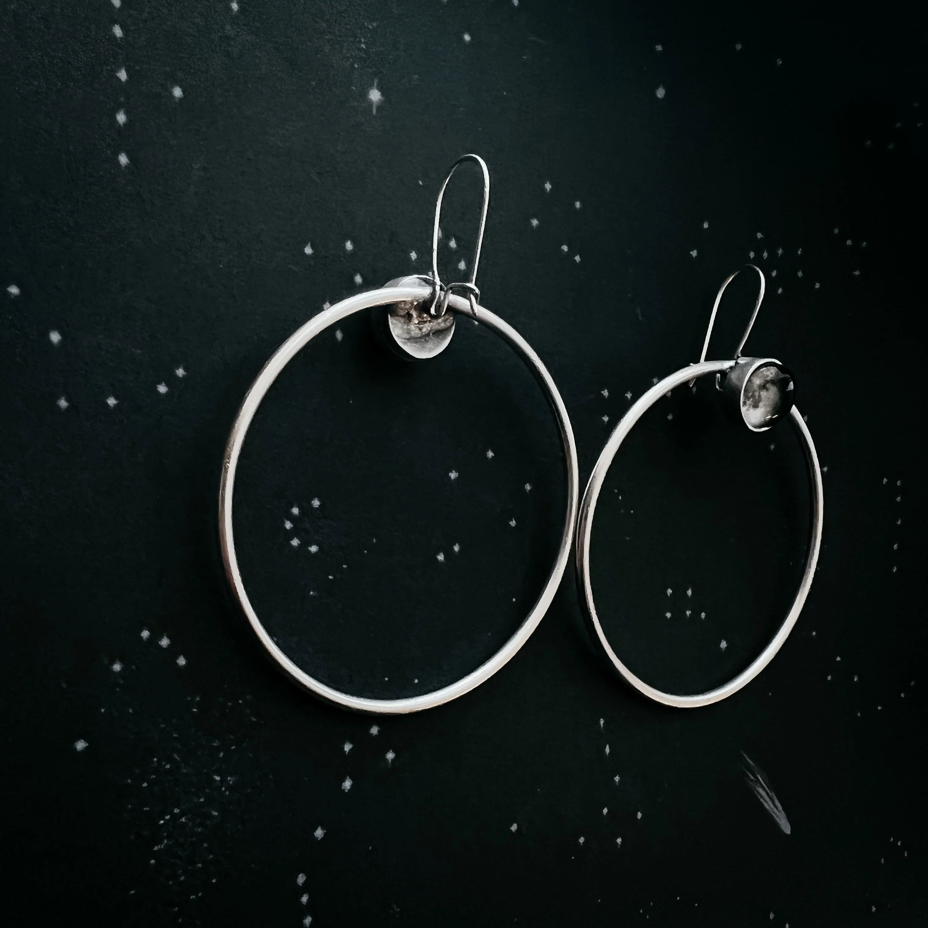 Pair of silver hoop earrings with latch backs on dark speckled background