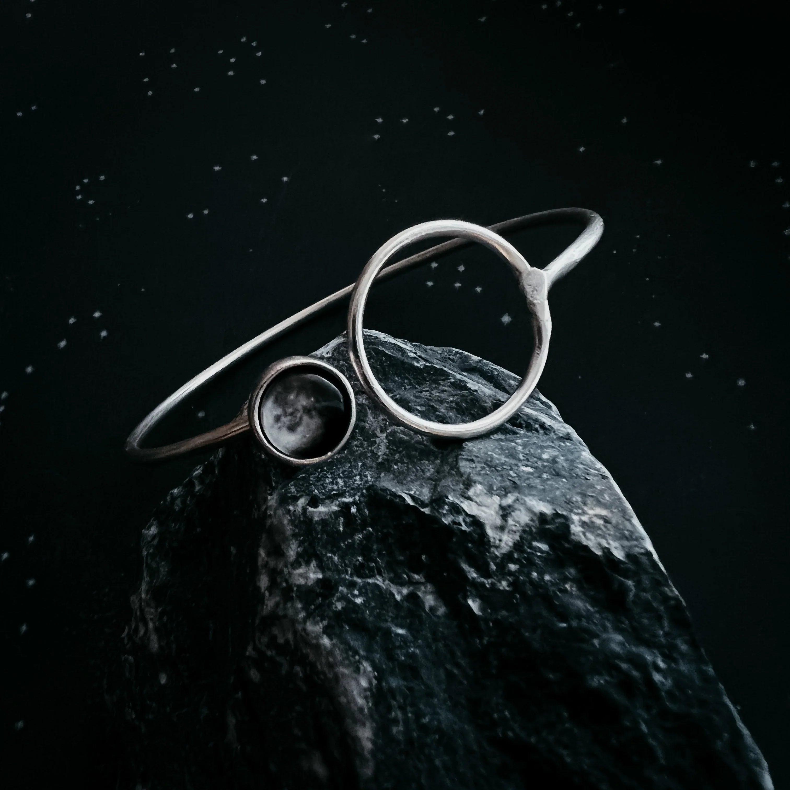 Cosmic-inspired silver bracelet with celestial design, displayed on dark rock, Qu!rk Boutique jewelry