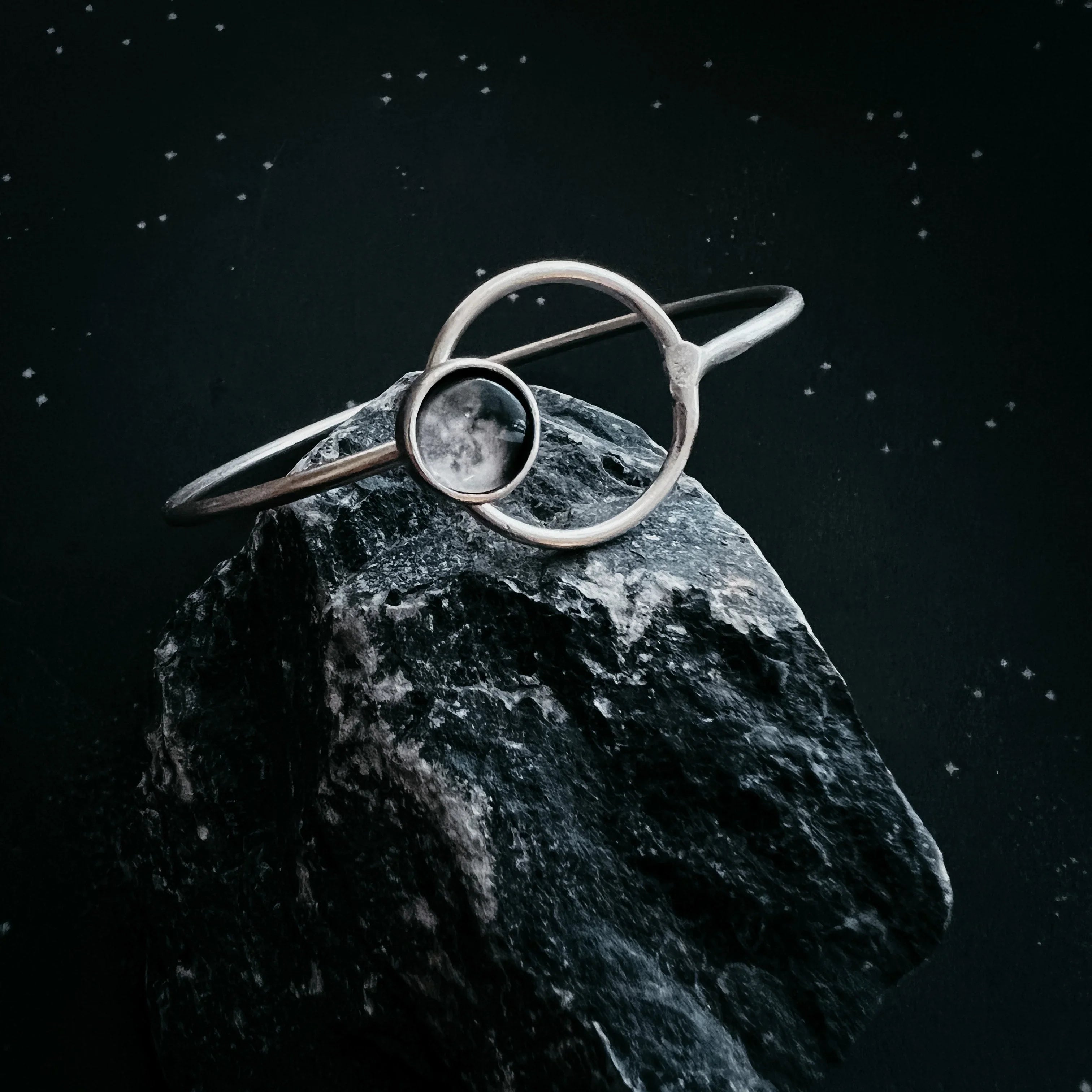 Cosmic silver bracelet with moonstone accent on dark rock, Qu!rk artist-designed jewelry