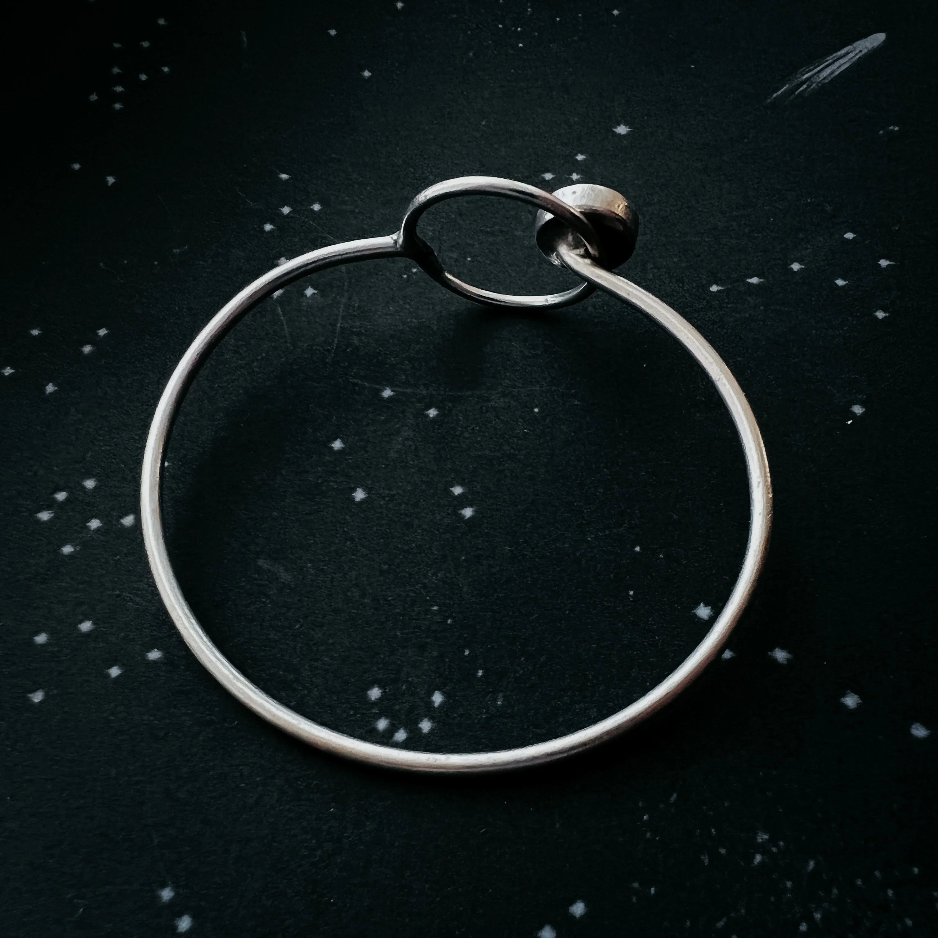 Minimalist silver bangle bracelet on a star-speckled cosmic background at Qu!rk Boutique