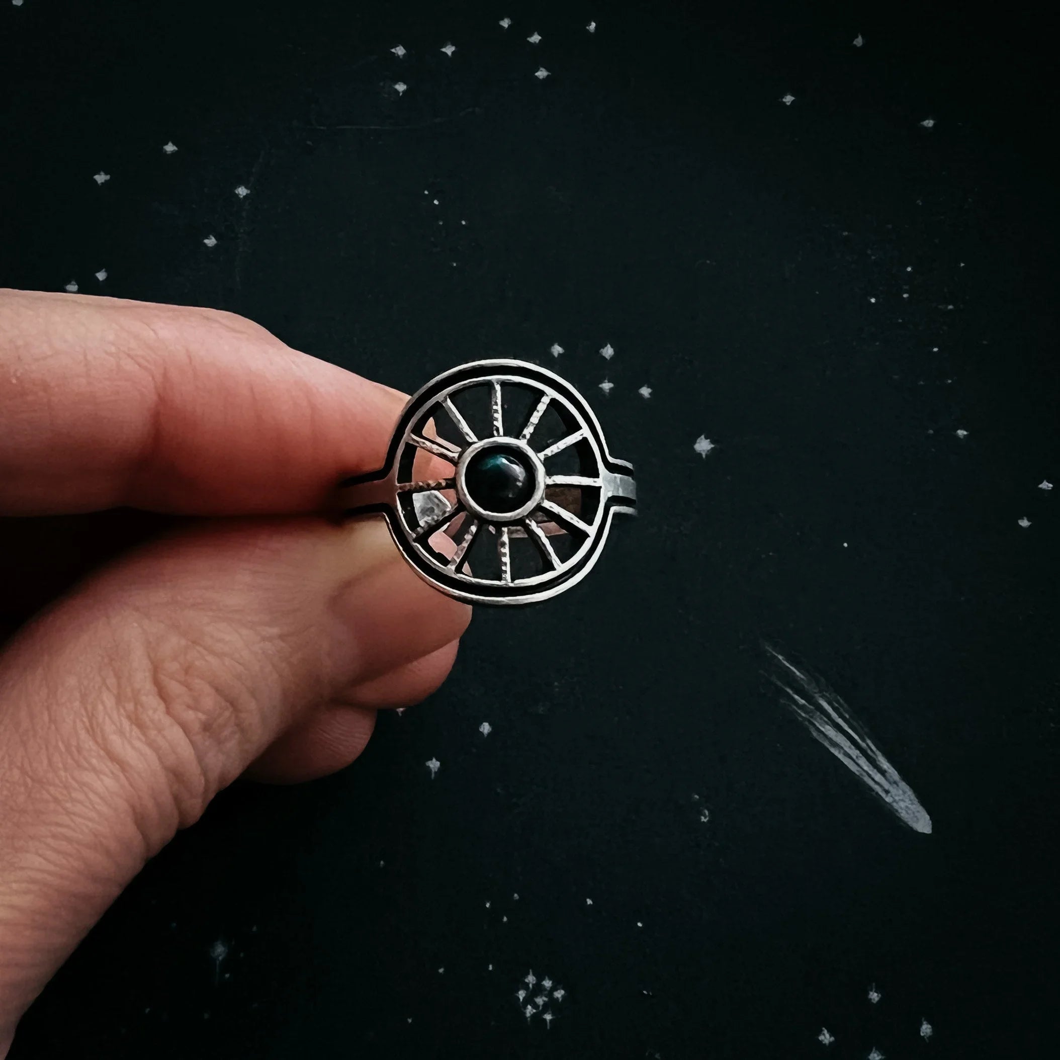 Hand holding cosmic-inspired silver ring with dark gemstone, stars in the background