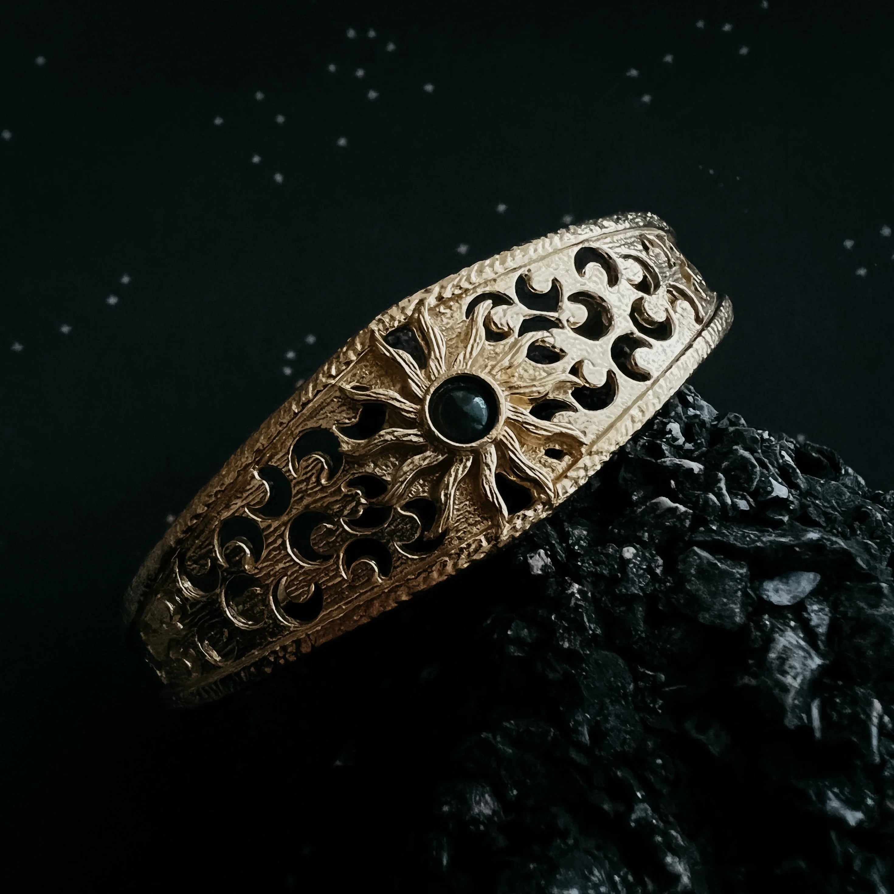 Gold bracelet with black gemstone sun and moon cutout design on black textured surface