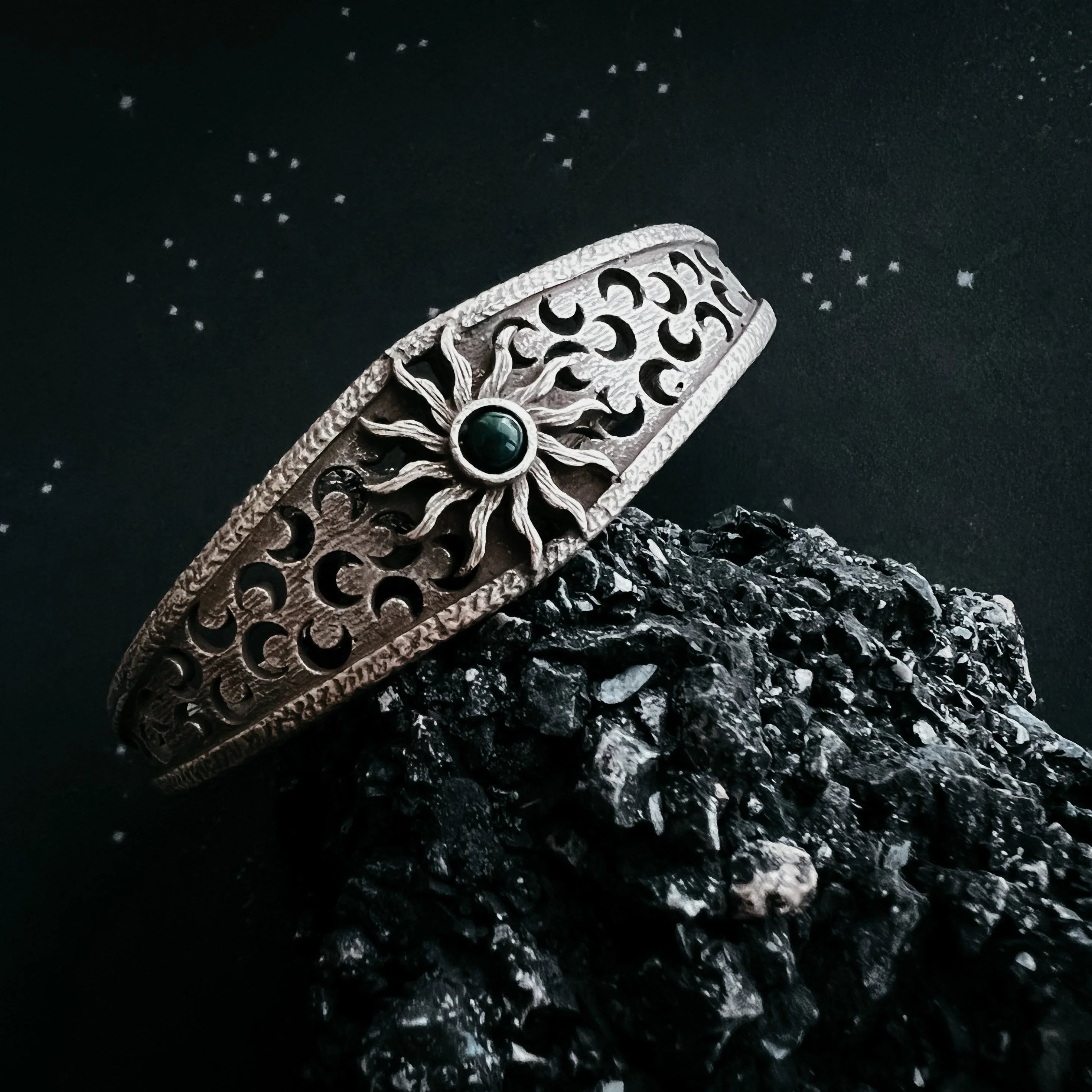 Silver bracelet with sun centerpiece and crescent moon cutouts on black textured rock