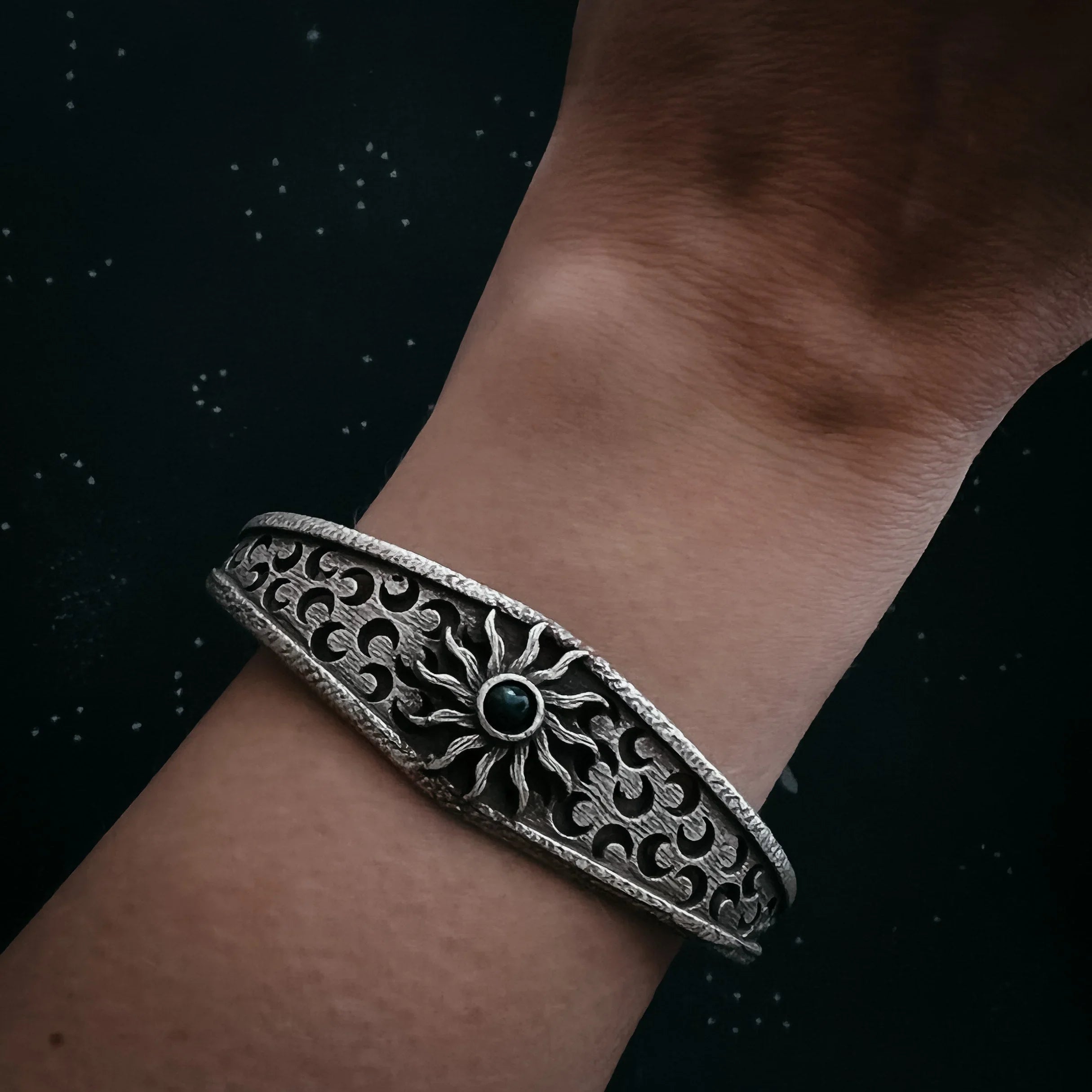 Silver bracelet with sun design and black stone on wrist against black background