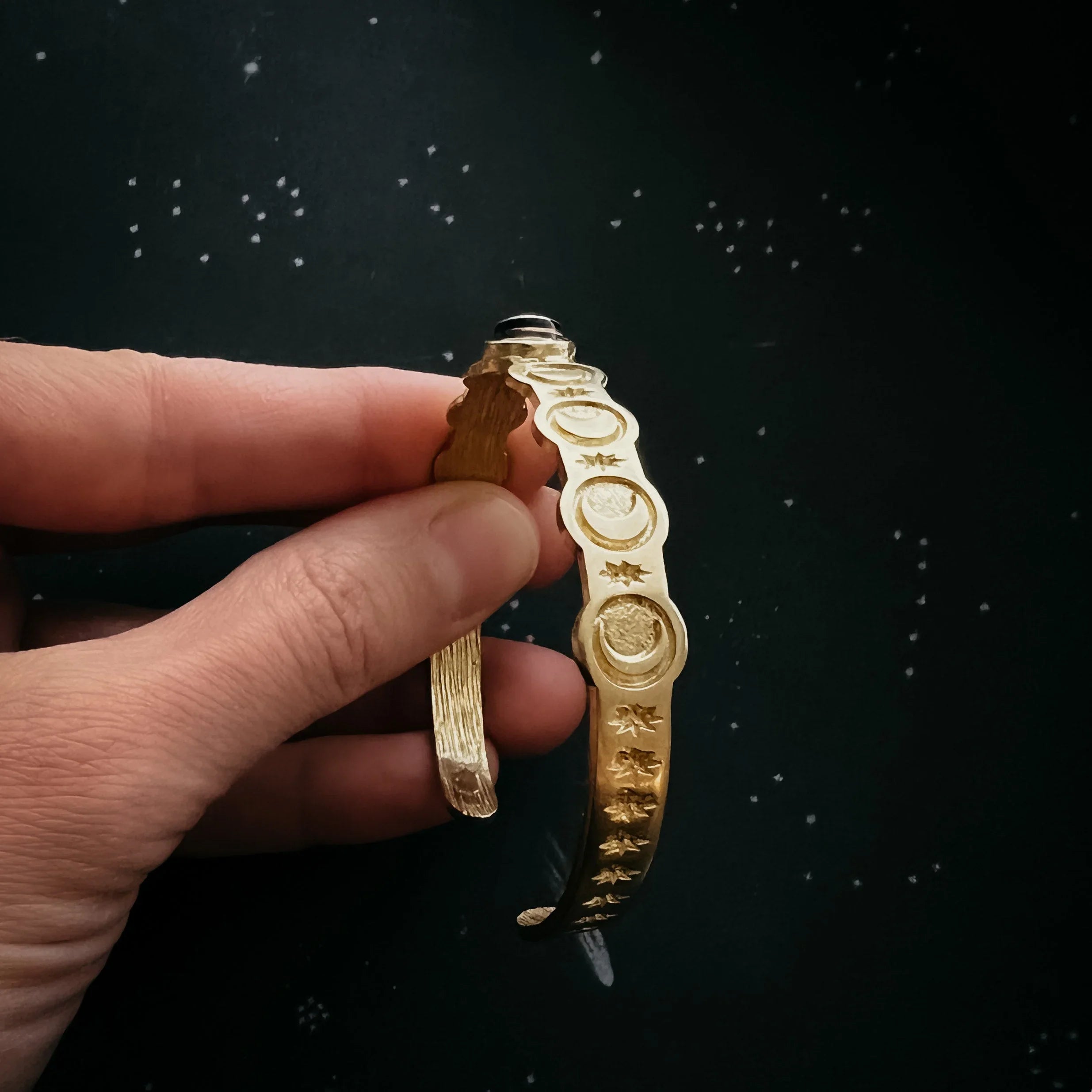 Hand holding gold celestial cuff bracelet with moon and star design on cosmic background