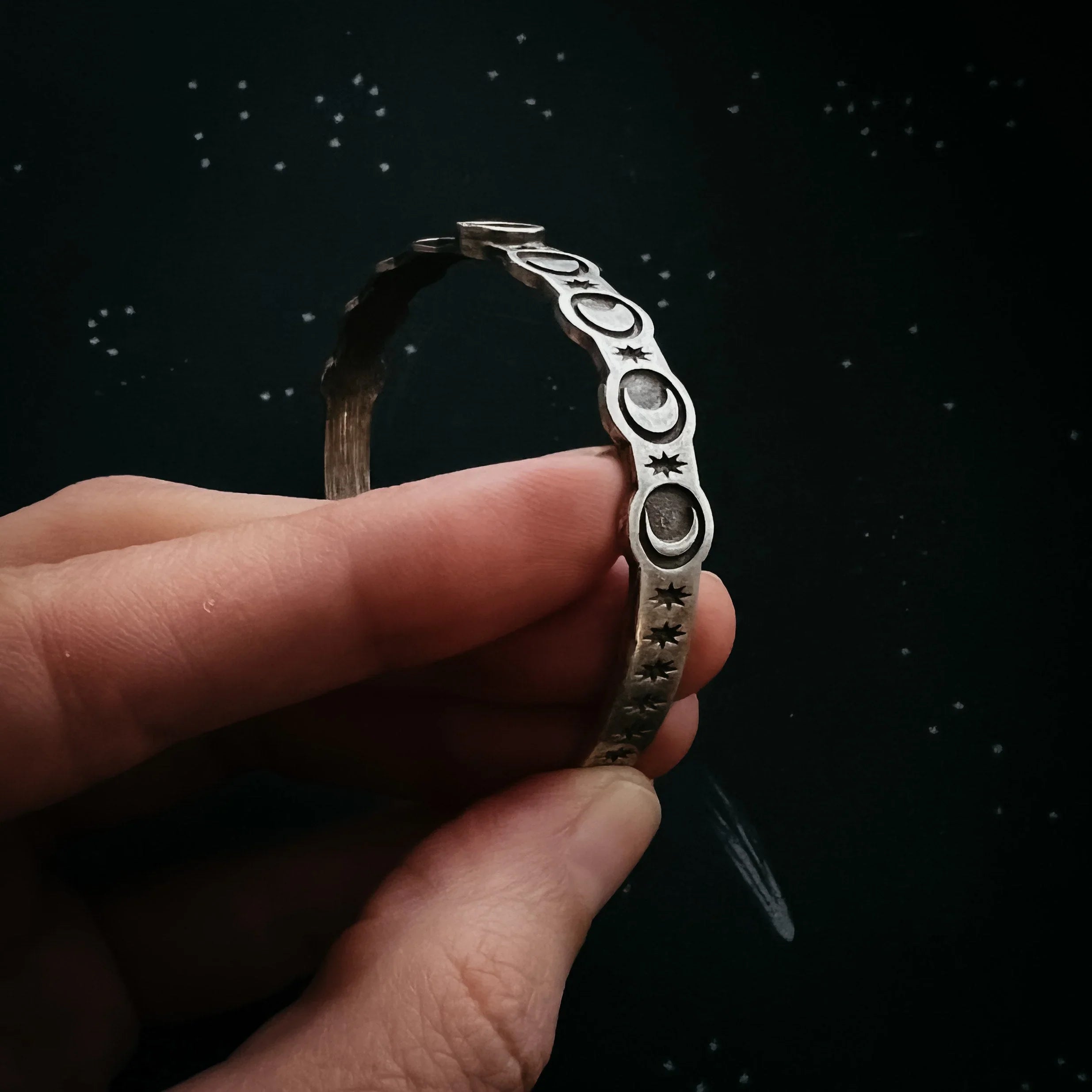 Hand holding silver bracelet with moon and star designs, cosmic jewelry from Qu!rk Boutique