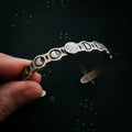 Hand holding a silver cuff bracelet with moon phases and gemstone, cosmic background