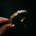 Hand holding gold moon phases cuff bracelet with gemstone, cosmic jewelry at Qu!rk Boutique