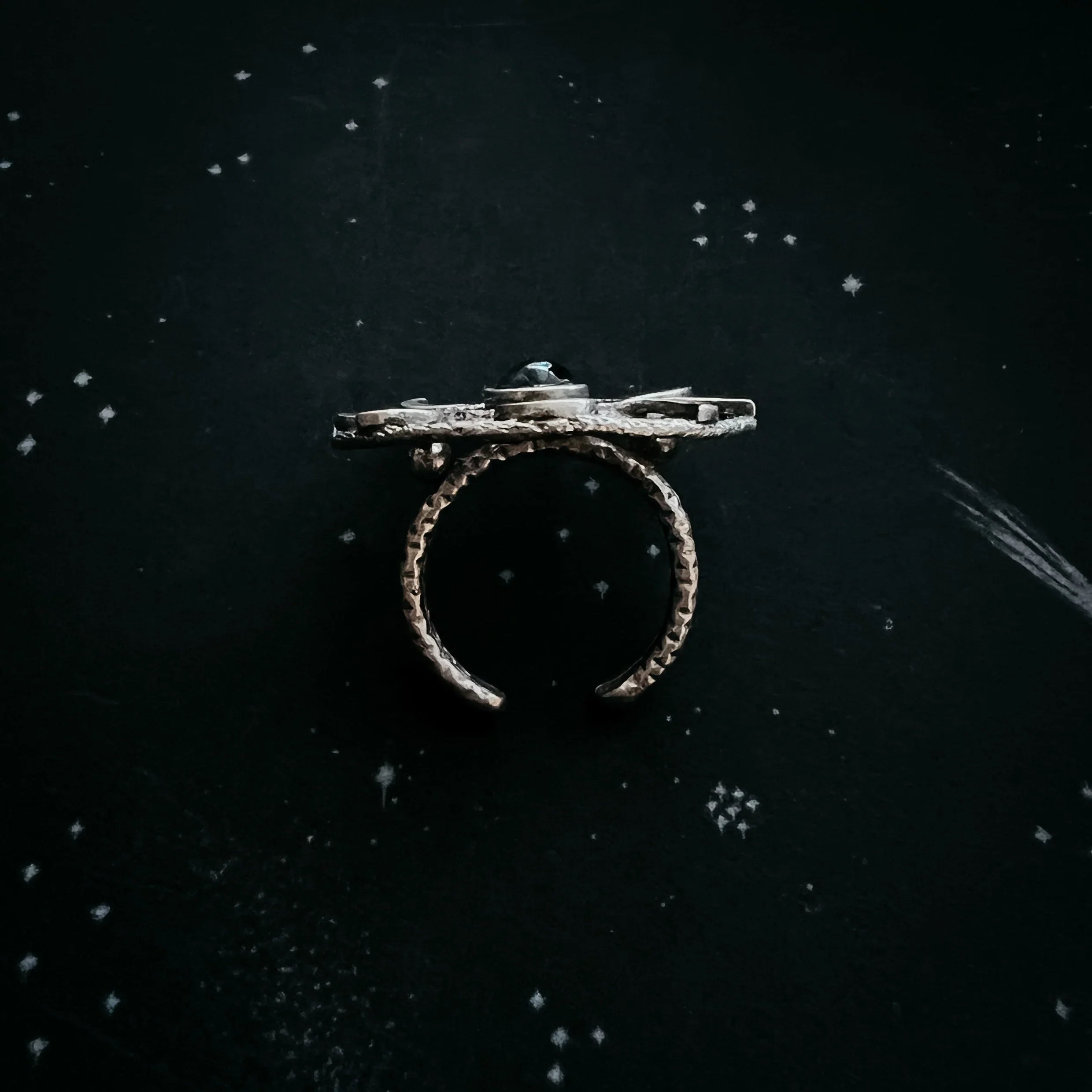 Rustic silver open band ring with a flat top, displayed on a black surface with white star-like speckles