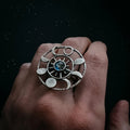 Hand wearing silver ring with celestial design featuring phases of the moon and a central blue stone