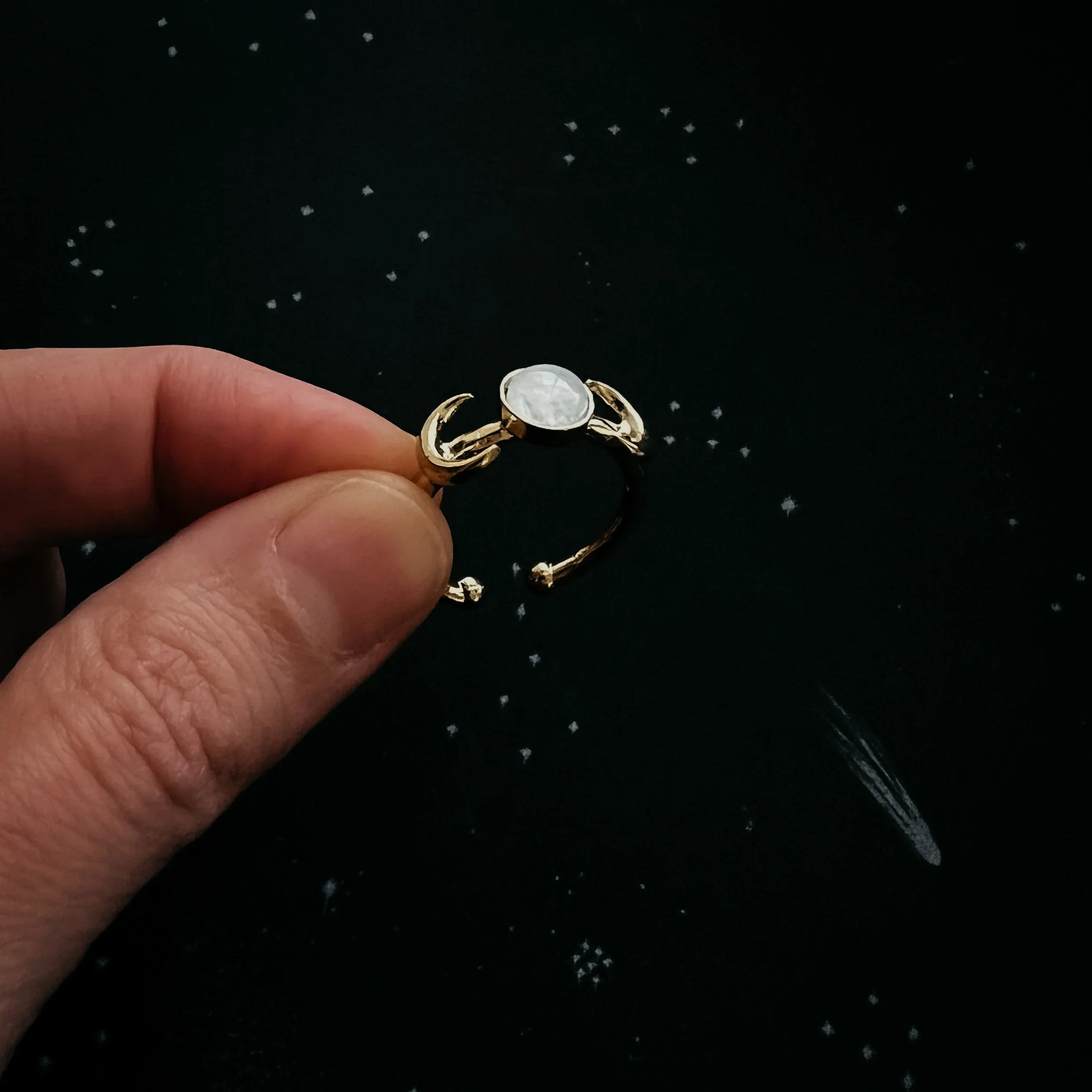 Gold moonstone ring with crescent moon design held by hand, cosmic background, Qu!rk Boutique