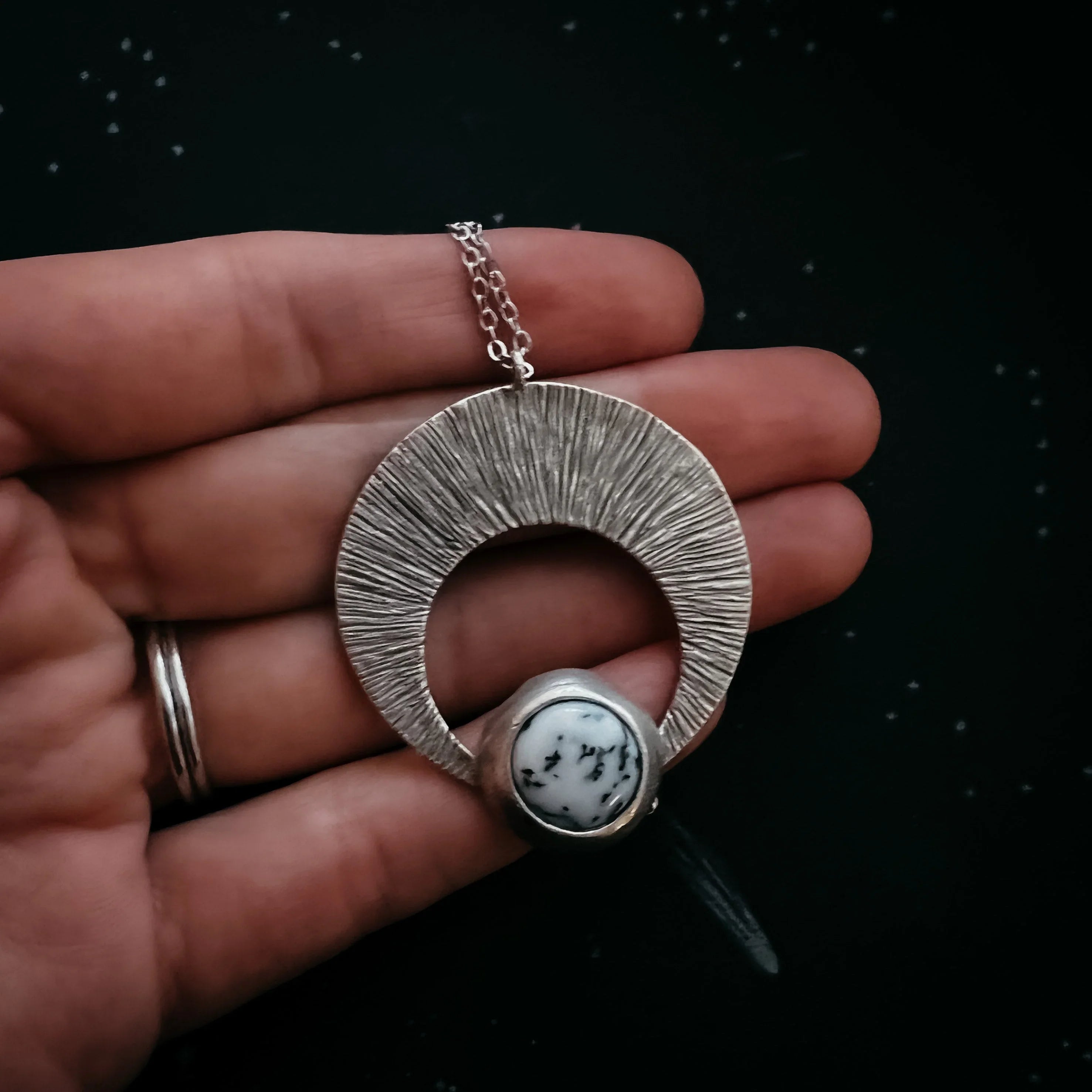 Hand holding artisan silver pendant necklace with dendritic white stone, cosmic jewelry