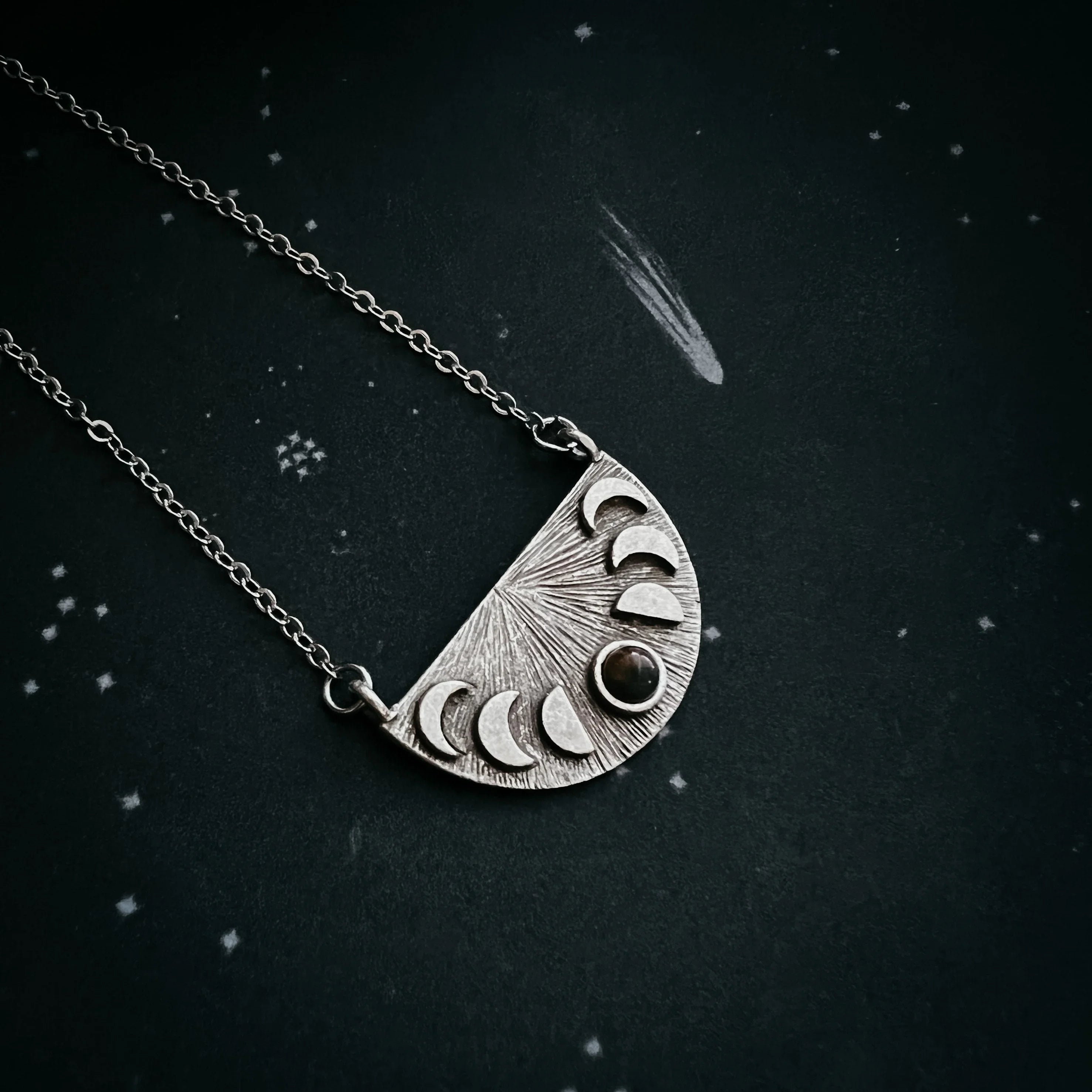 Silver necklace with crescent moon phases and a black stone pendant on starry background