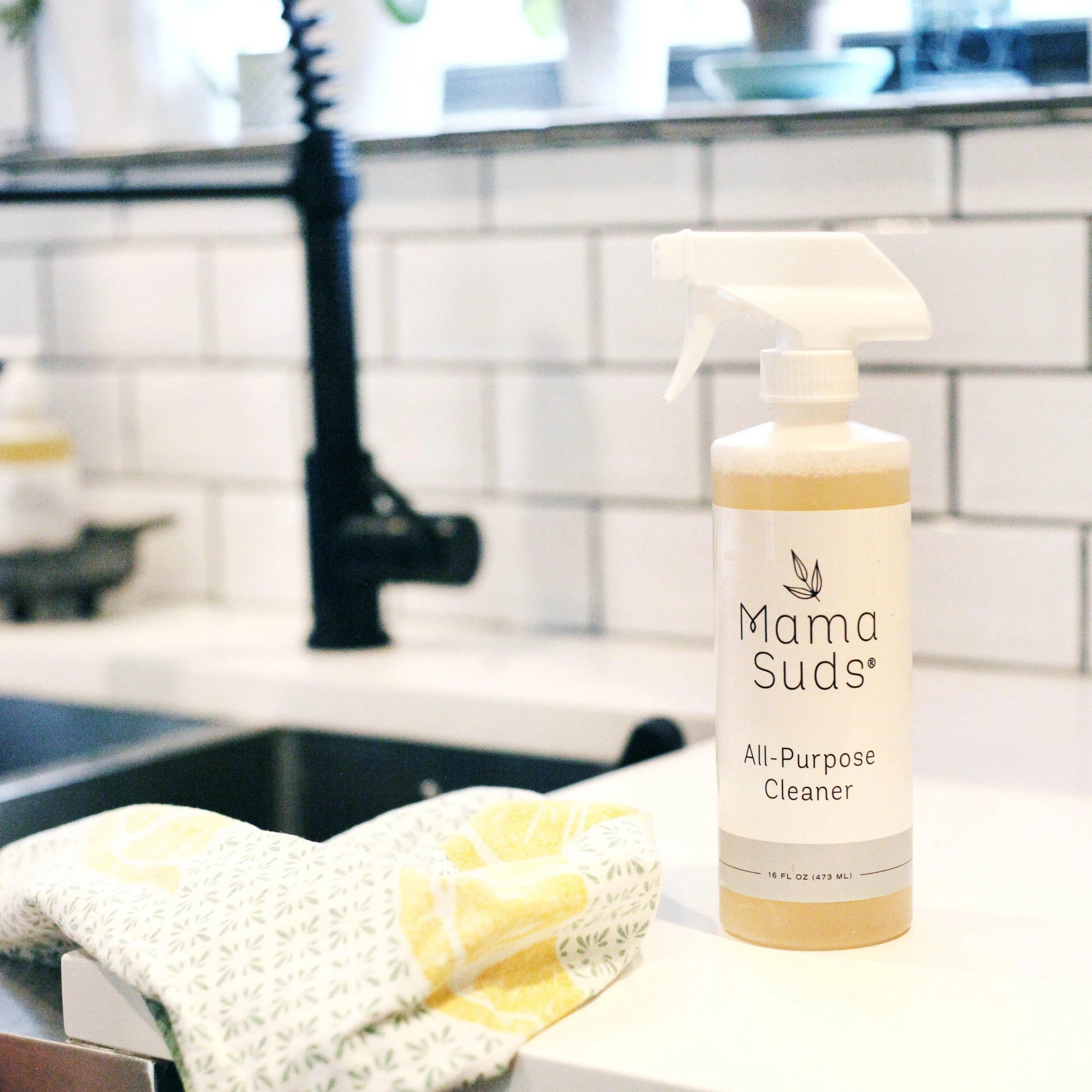 Mama Suds all-purpose cleaner bottle on a white kitchen counter with a patterned towel and tile backsplash
