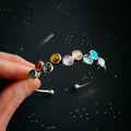 Hand holding silver bracelet with multicolored polished gemstone beads on dark starry background