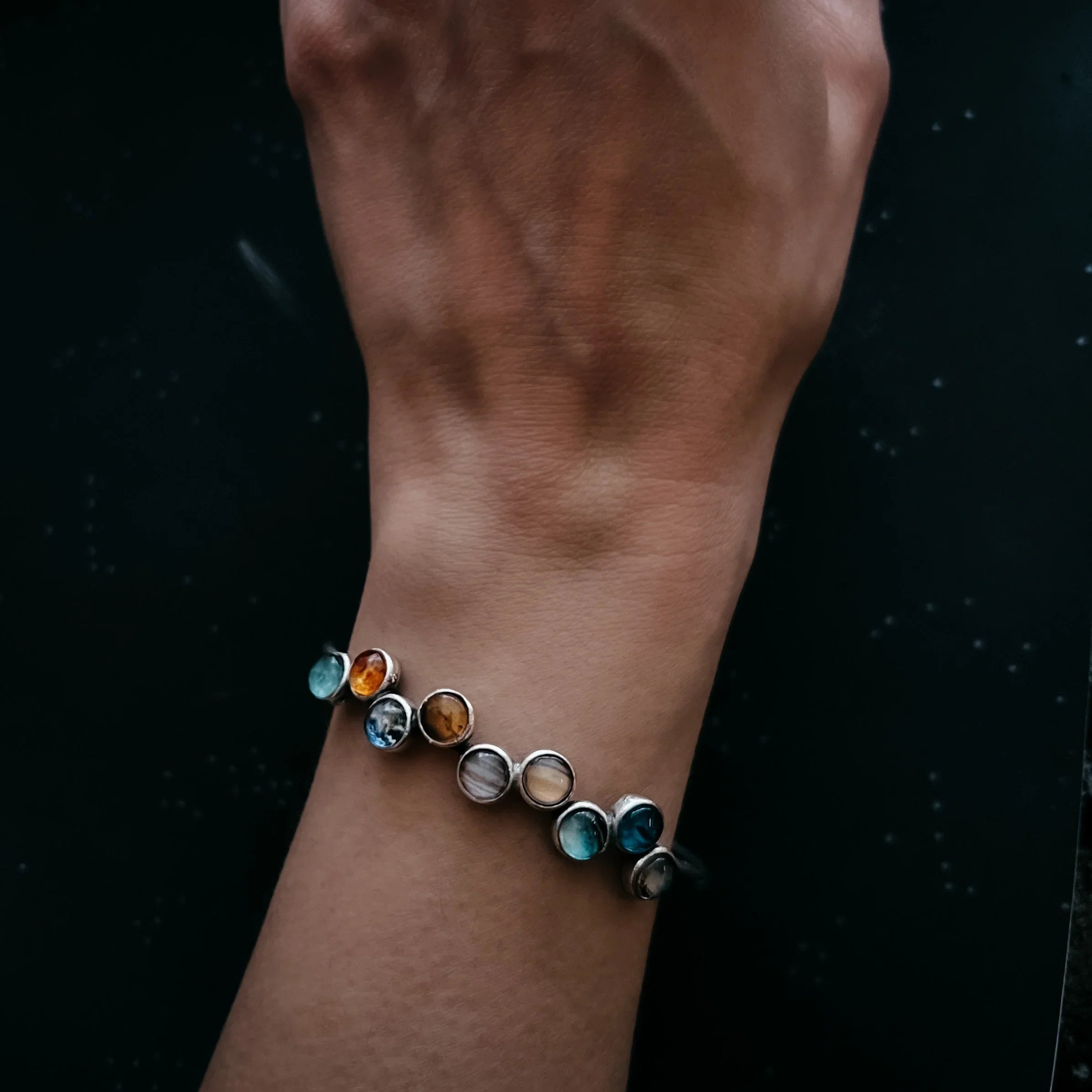 Close-up of wrist wearing a multicolor gemstone silver bracelet on dark background