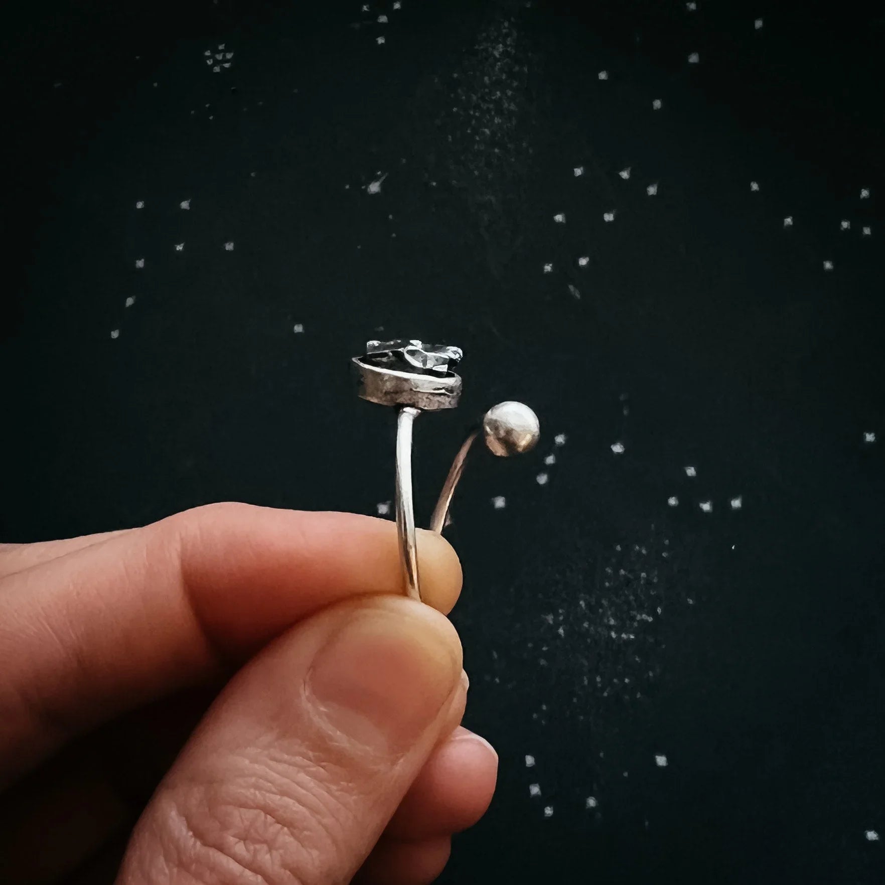 Hand holding artist-designed silver open ring with celestial details on black starry background