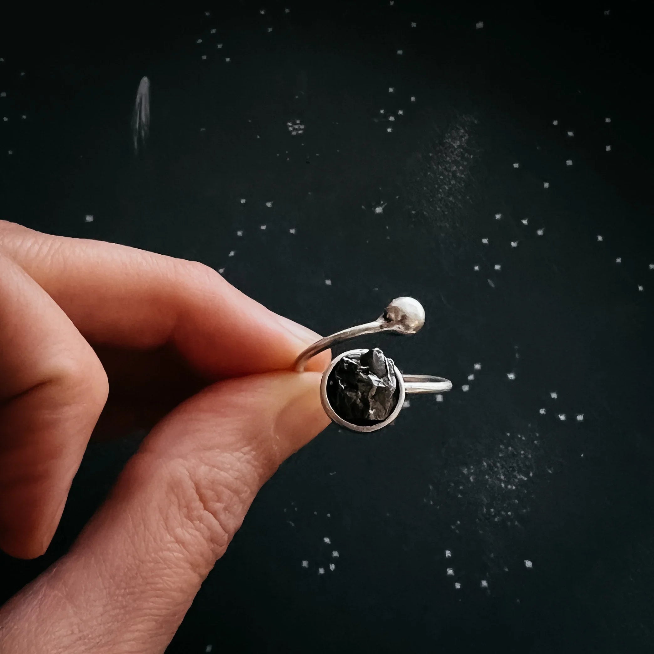 Hand holding silver cosmic-inspired adjustable ring with black stone, Qu!rk Boutique jewelry