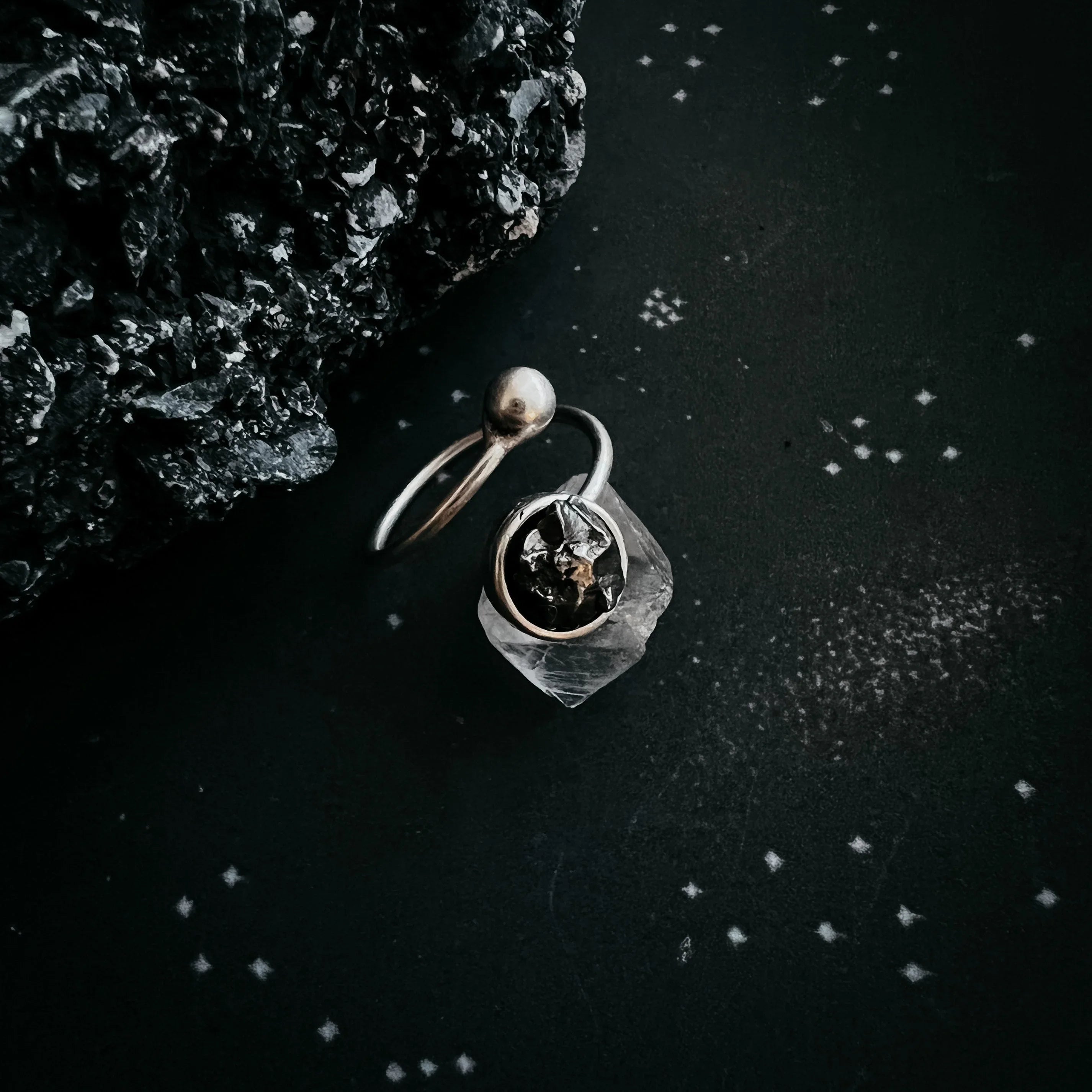 Cosmic-inspired silver ring with raw stone on dark star-patterned background, Qu!rk Boutique