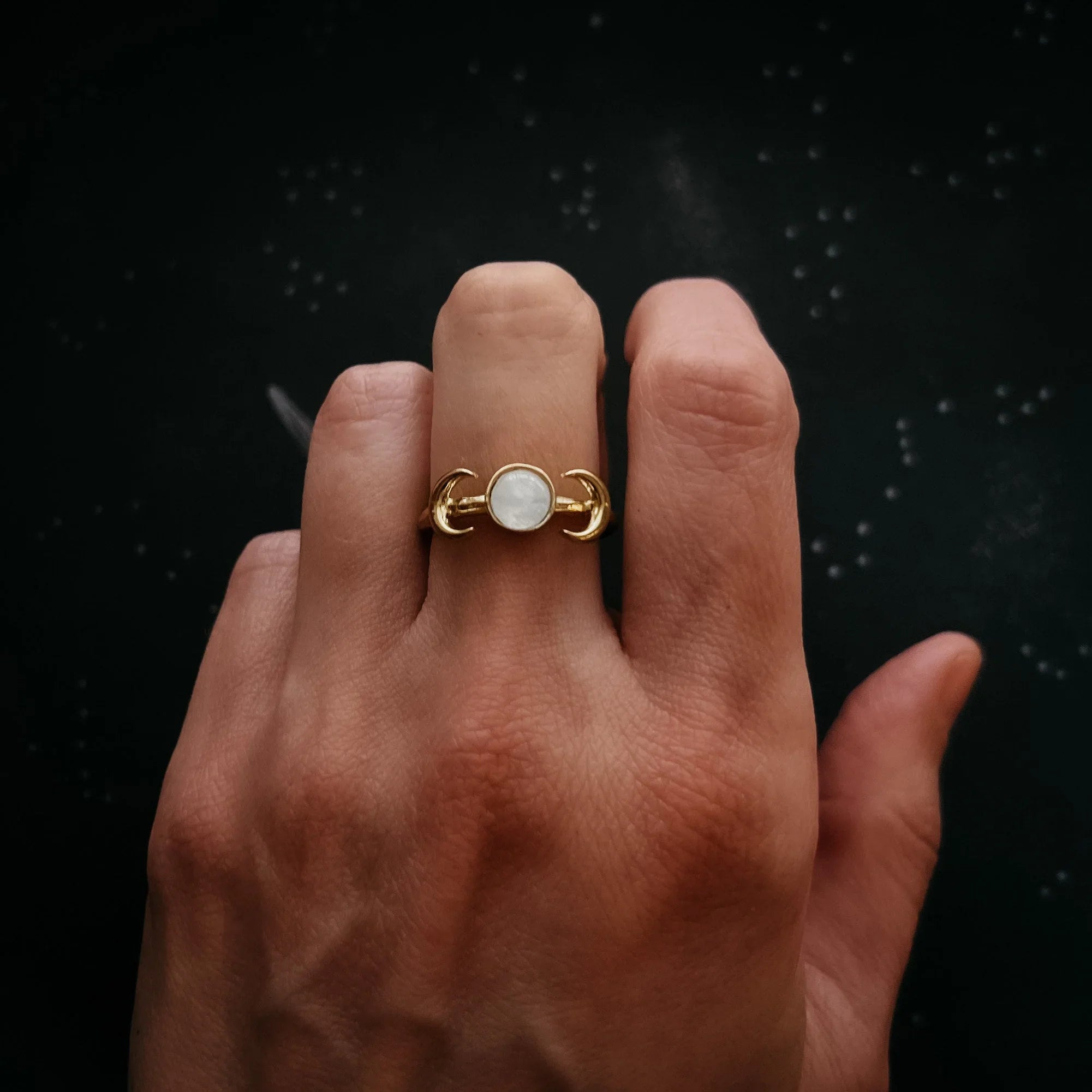 Hand wearing a gold moon phase ring with white stone, cosmic-inspired jewelry from Qu!rk Boutique