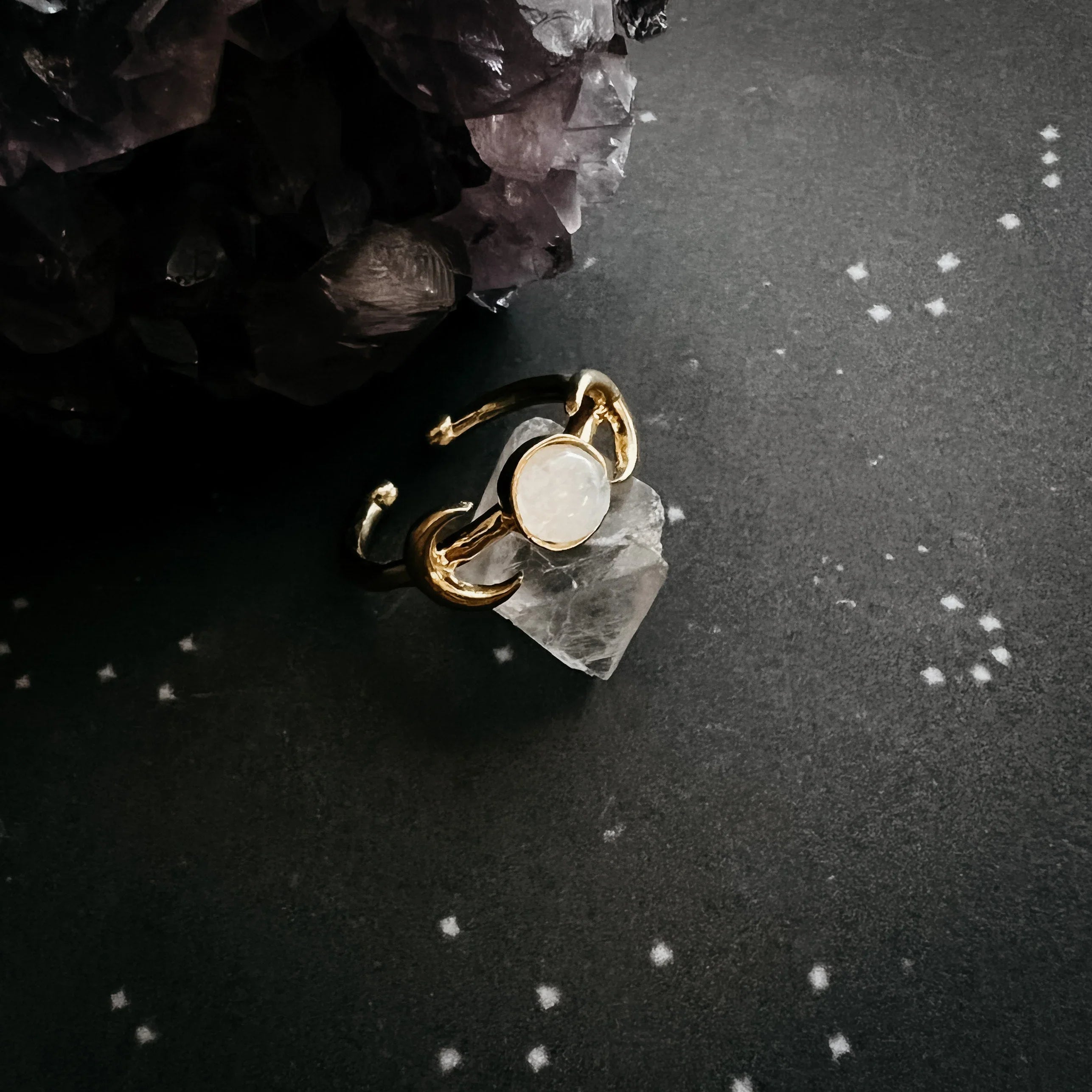 Gold ring with a round gemstone on a crystal, cosmic star-patterned backdrop, Qu!rk Boutique