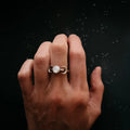 Hand wearing a celestial moon phase ring with pearl, cosmic starry background