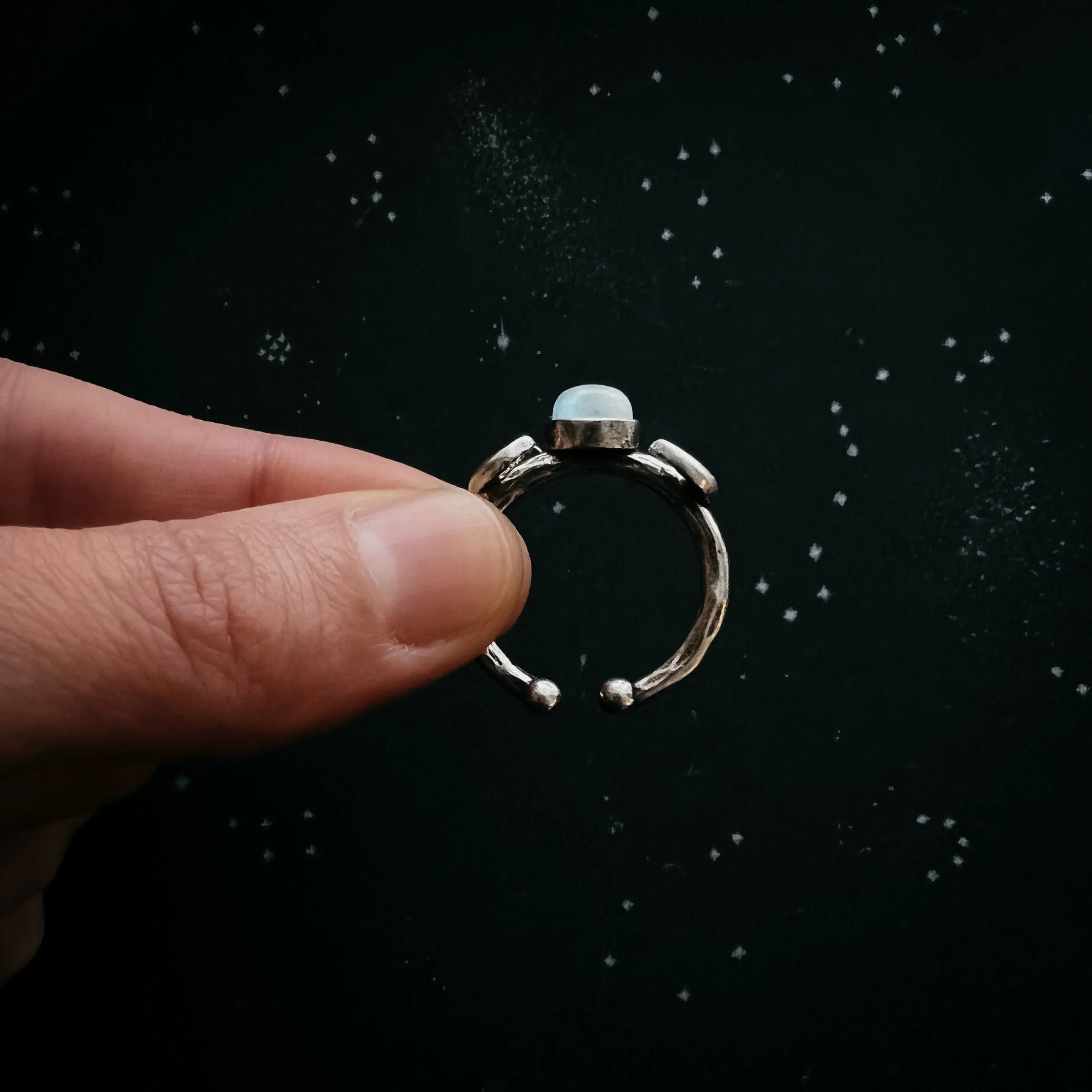 Hand holding a cosmic-inspired silver ring with gemstone, black starry background, Qu!rk Boutique