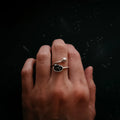 Hand wearing a silver open ring with one black stone and one silver bead on a dark background