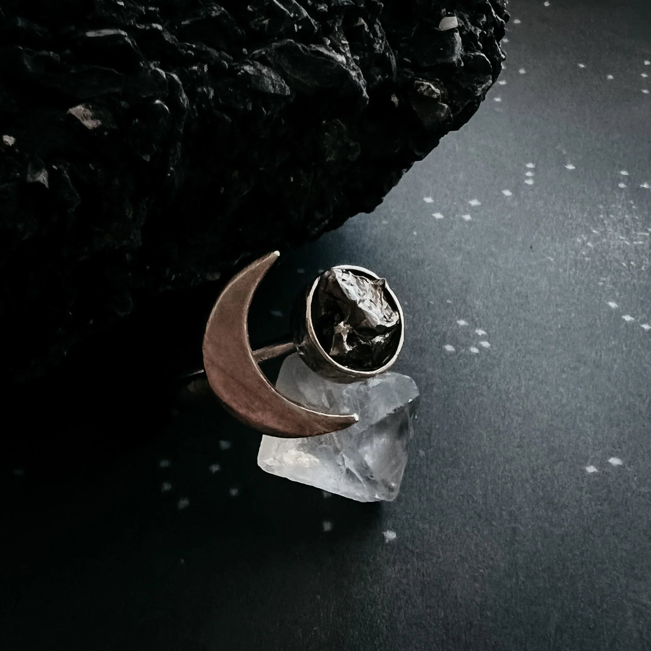 Handcrafted crescent moon ring with raw stone on dark textured surface with black rock