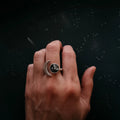 Hand wearing a silver moon and black stone celestial ring on a starry dark background
