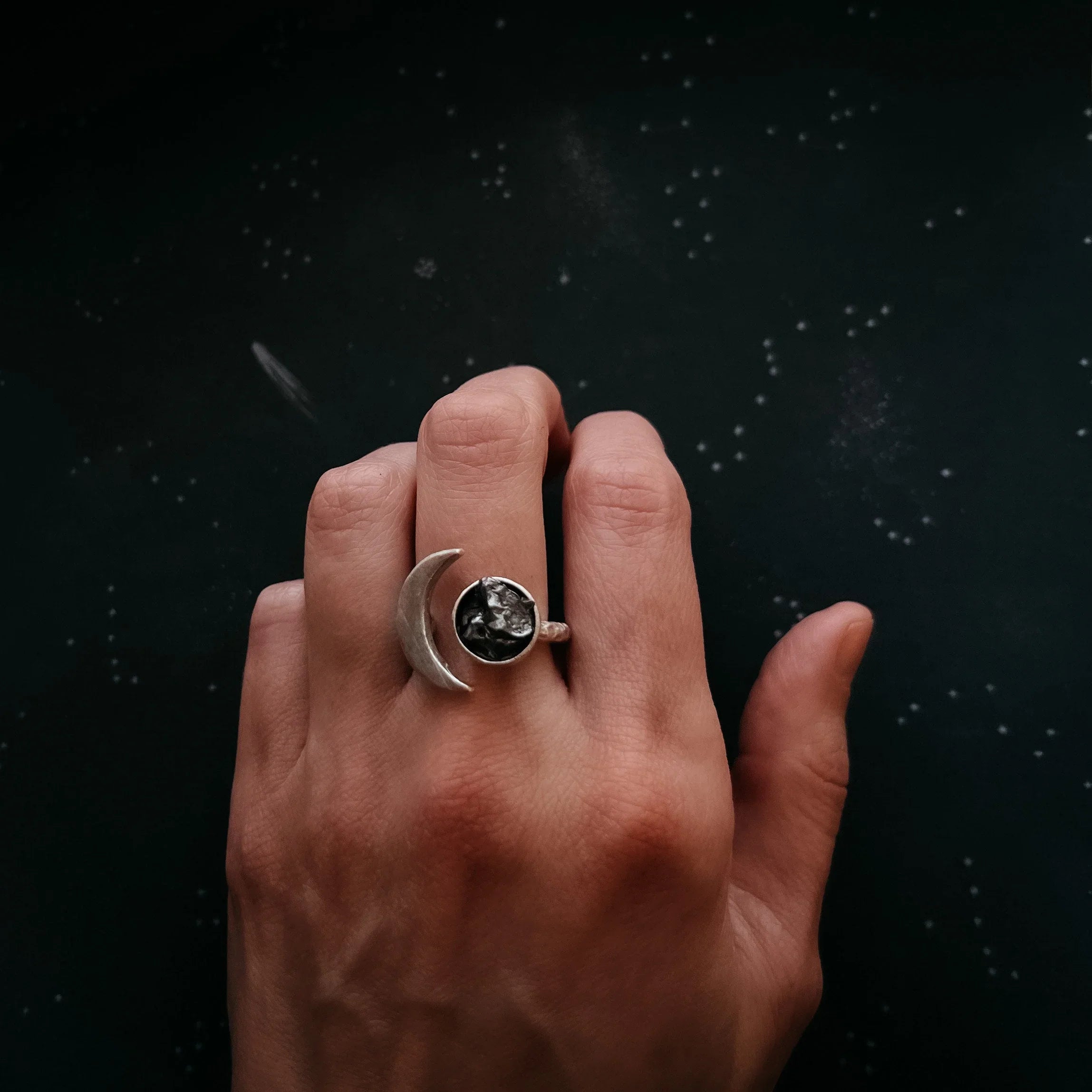Hand wearing a silver moon and black stone celestial ring on a starry dark background