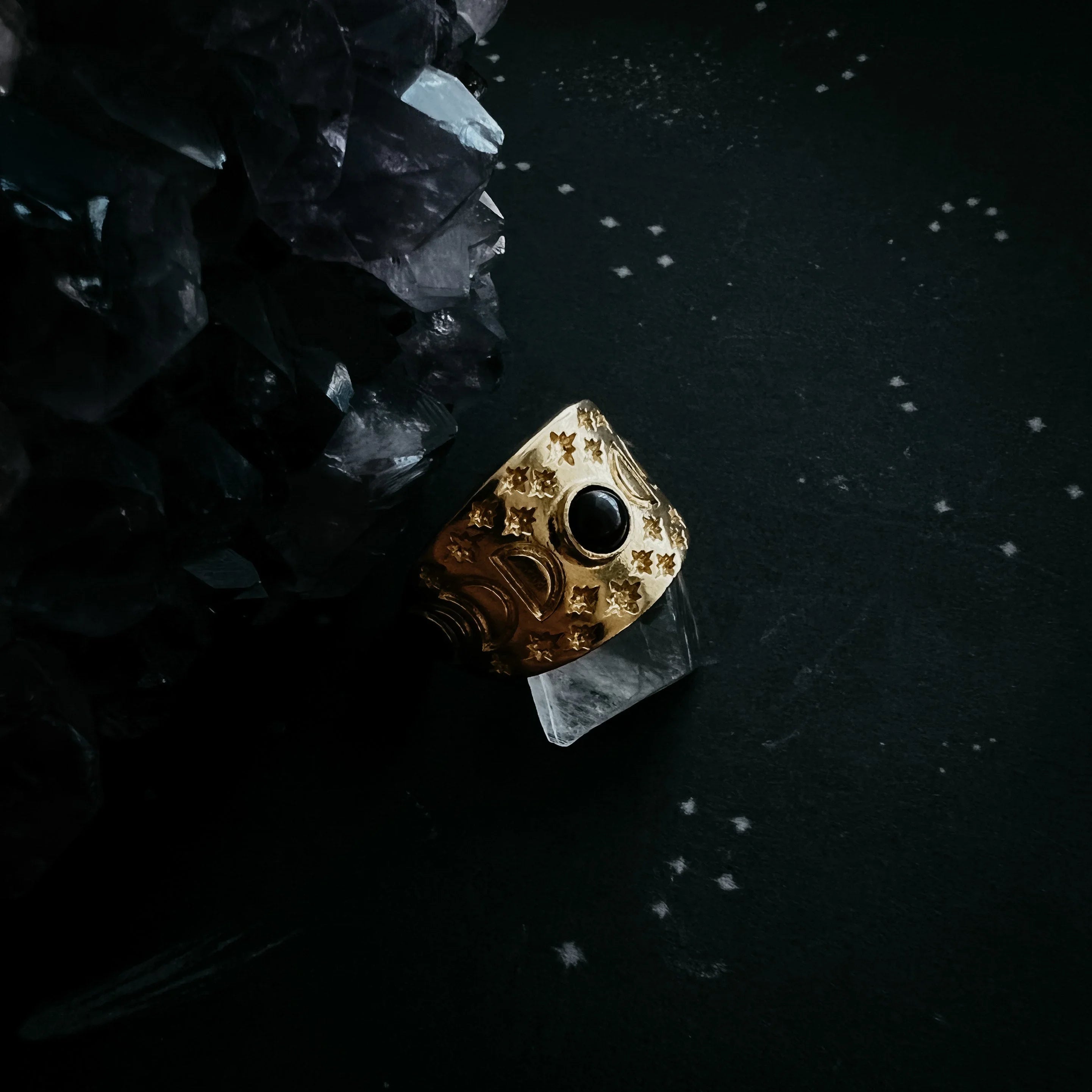 Gold celestial ring with black stone on dark background, cosmic jewelry at Qu!rk Boutique