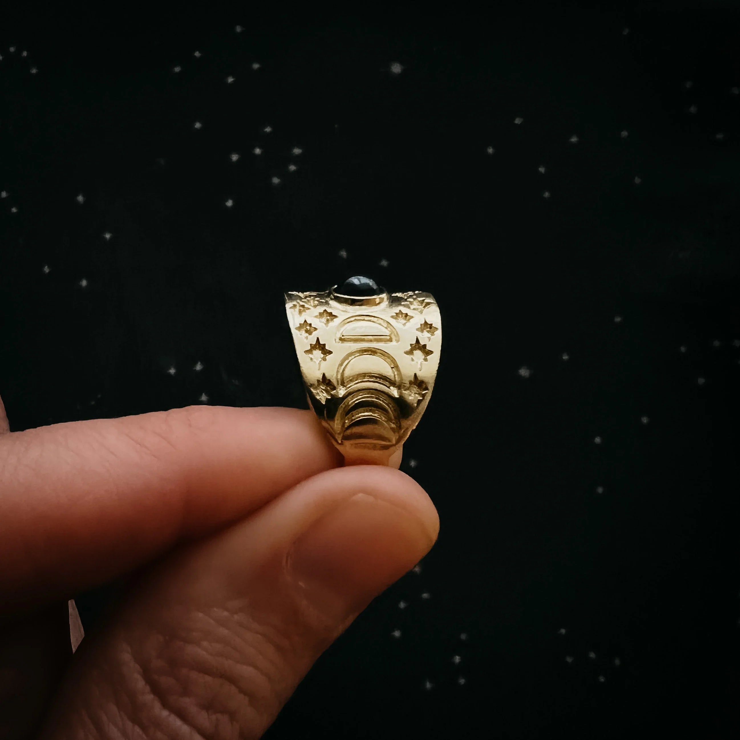Hand holding gold cosmic ring with moon phases and star designs, Qu!rk Boutique jewelry.