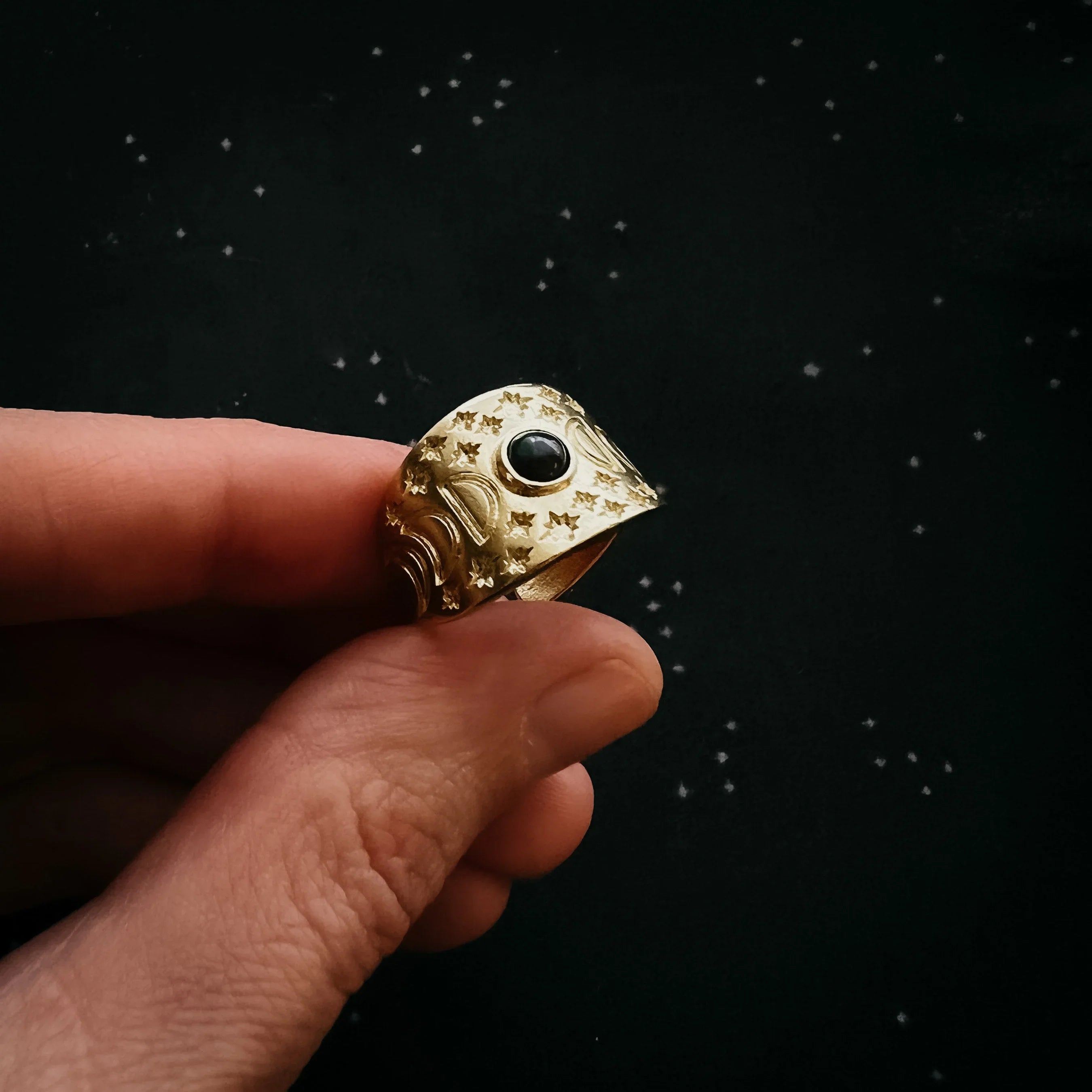 Hand holding cosmic-themed gold ring with star engravings and black stone, Qu!rk Boutique jewelry