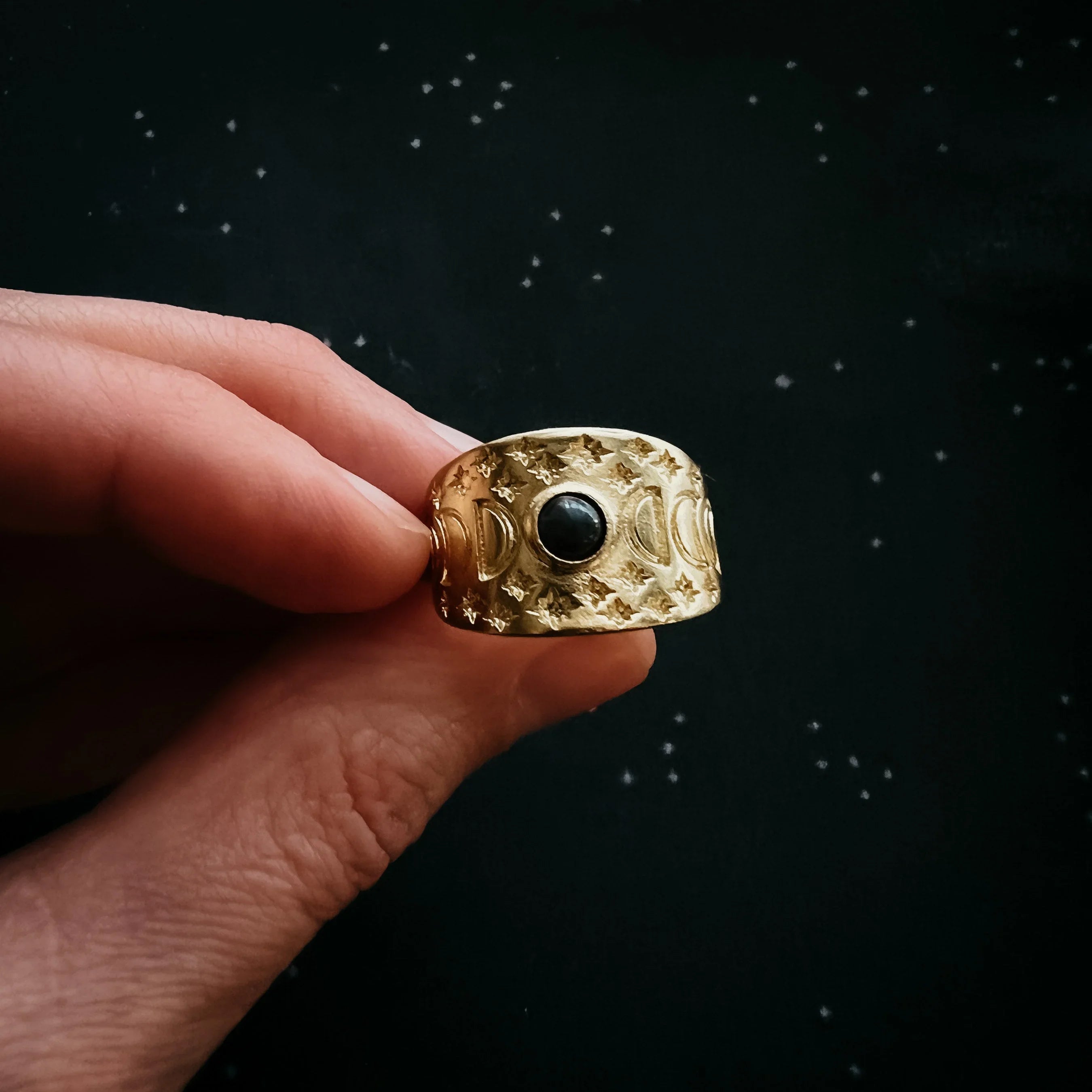Hand holding gold moon phase ring with black stone, cosmic design from Qu!rk Boutique