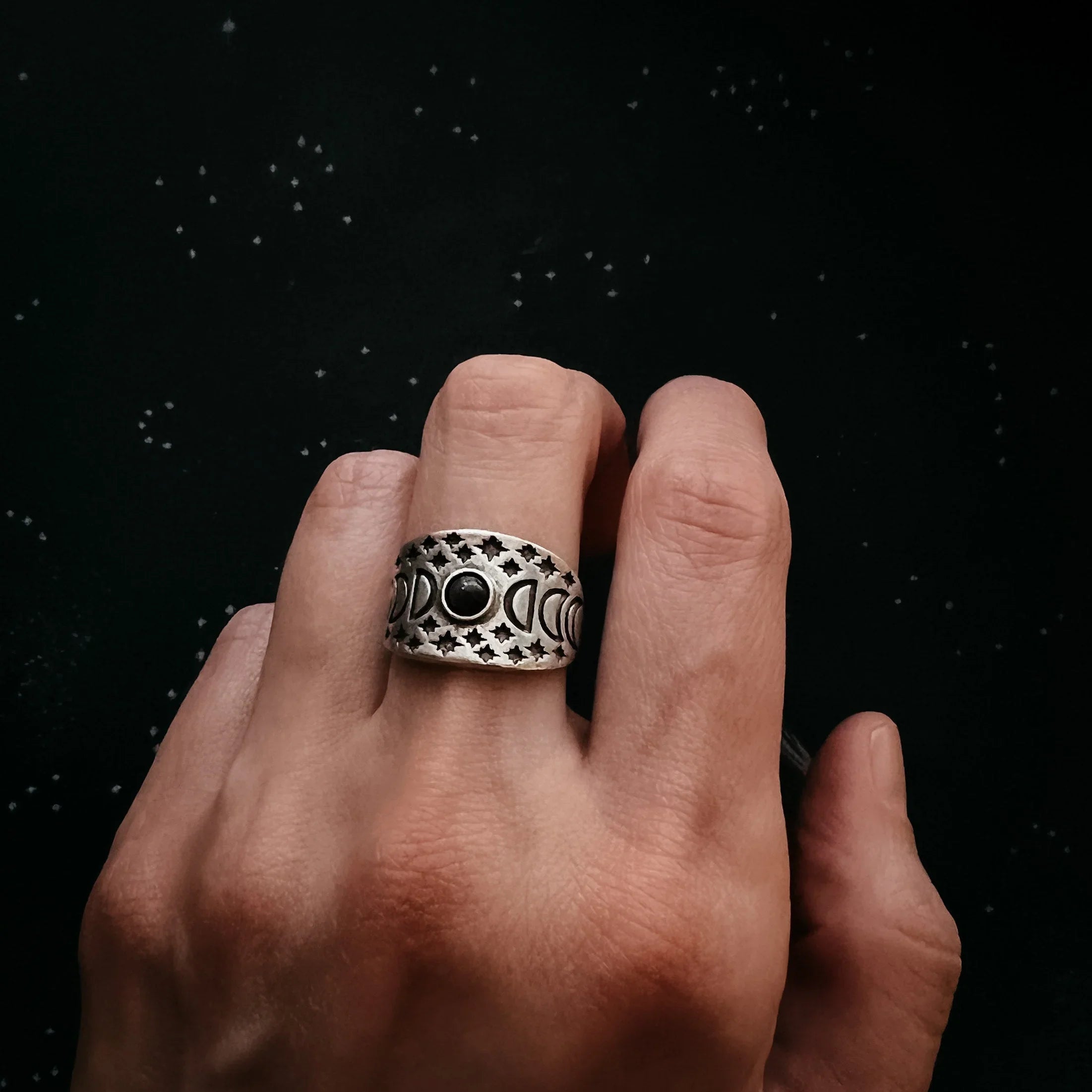 Hand wearing artist-designed silver moon phase ring with star details, cosmic background