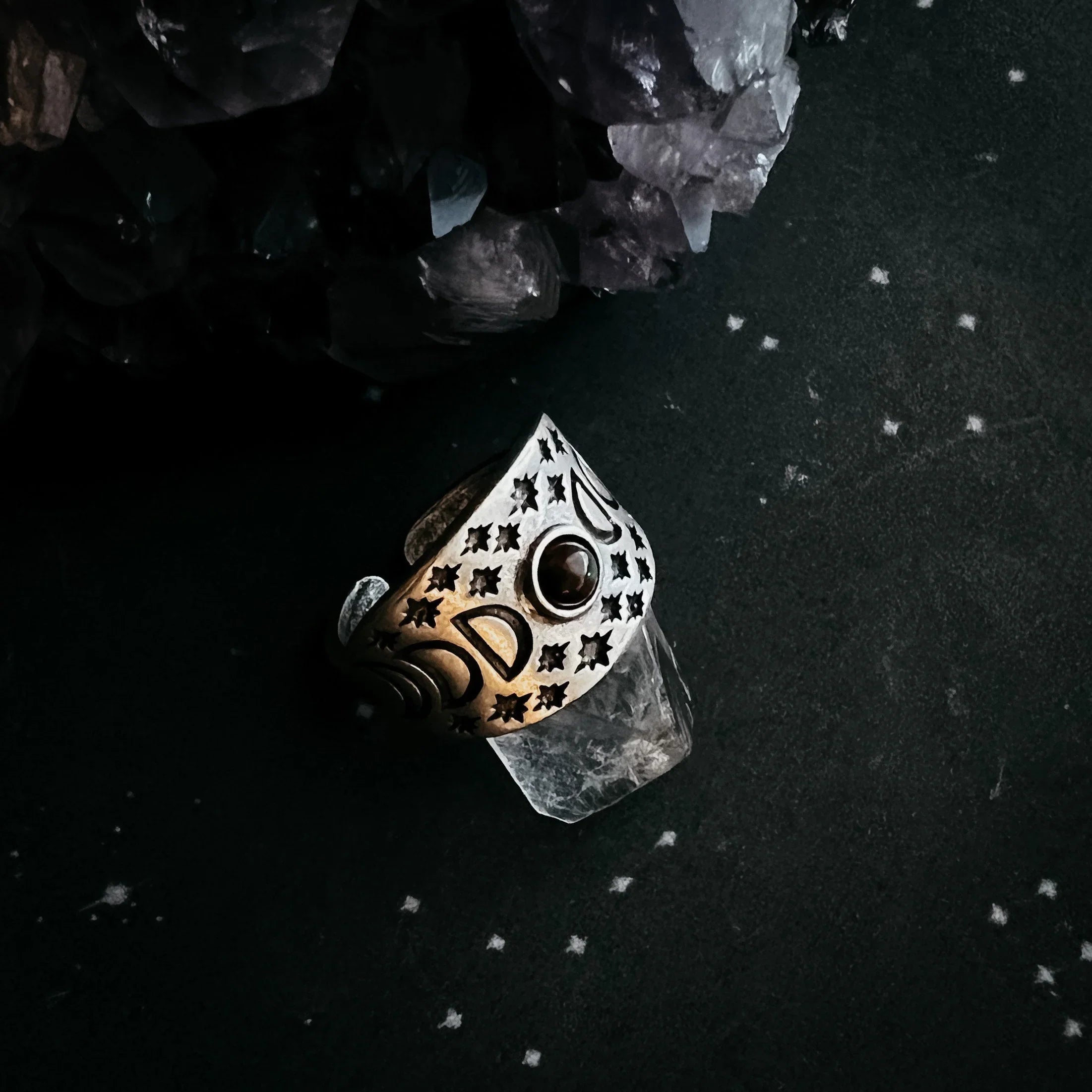 Cosmic-themed artisan ring with moon and stars, displayed on crystal beside amethyst cluster