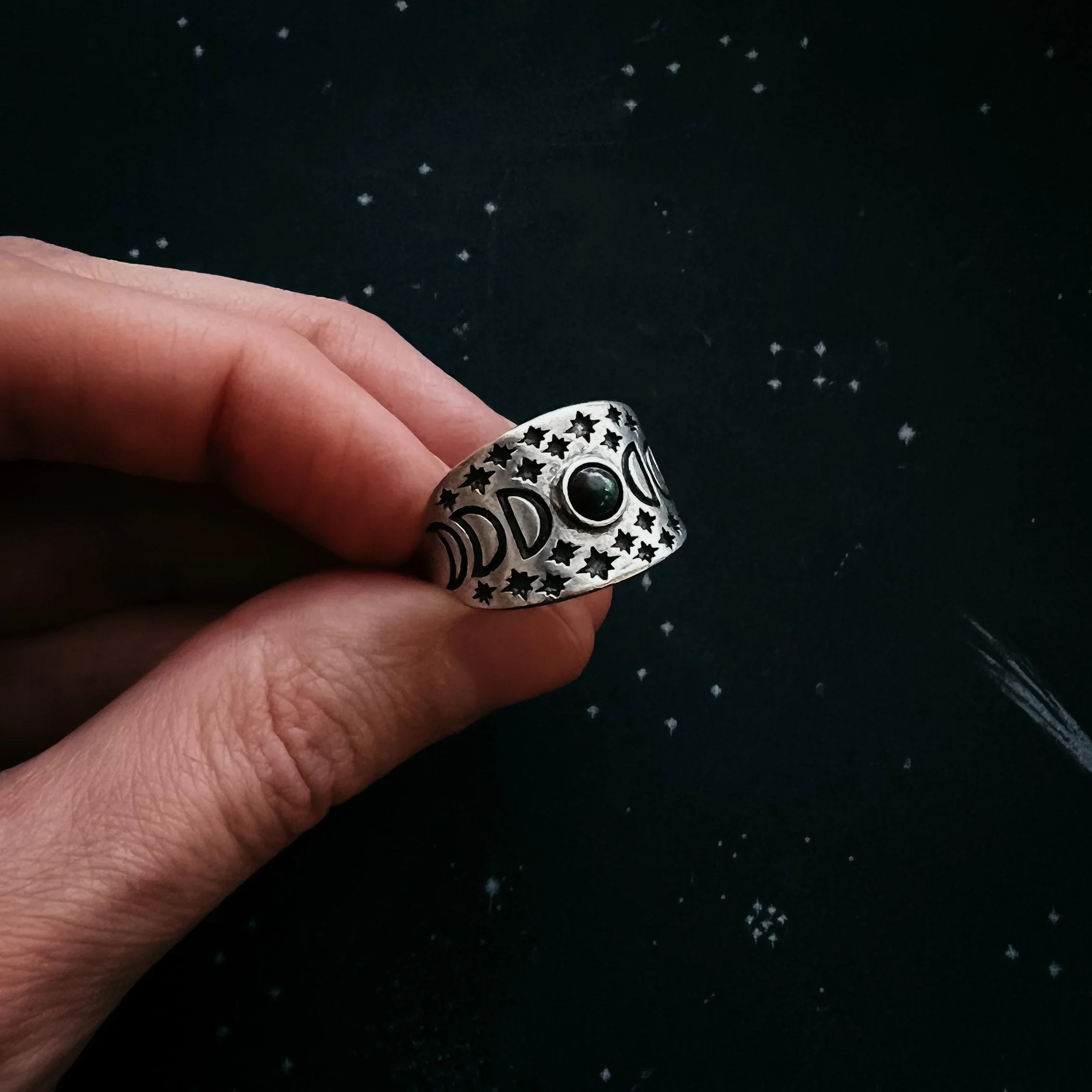 Hand holding silver cosmic-themed ring with moon phases and black stone, cosmic gift jewelry