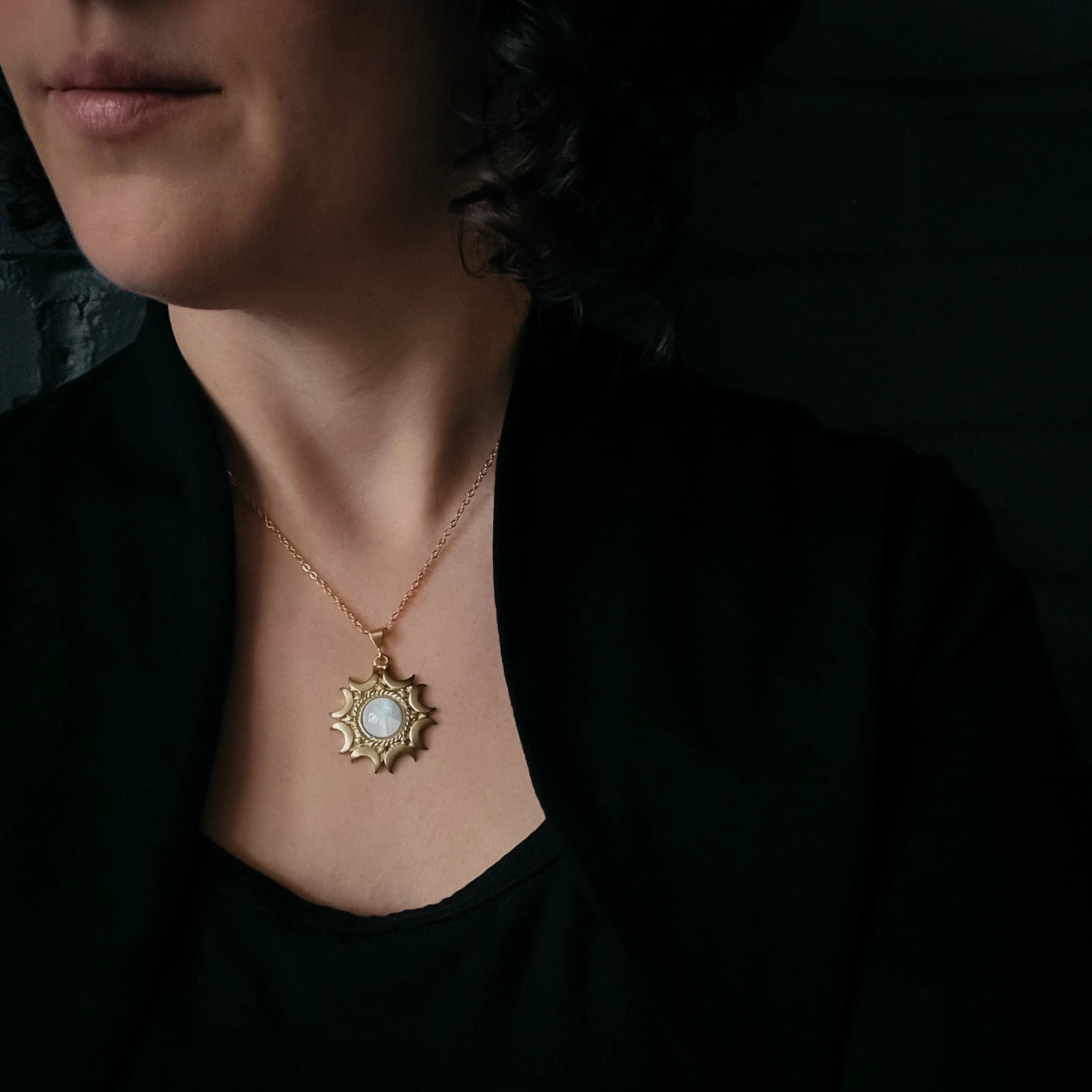 Close-up of a woman wearing a gold sun-shaped pendant necklace with a circular centerpiece