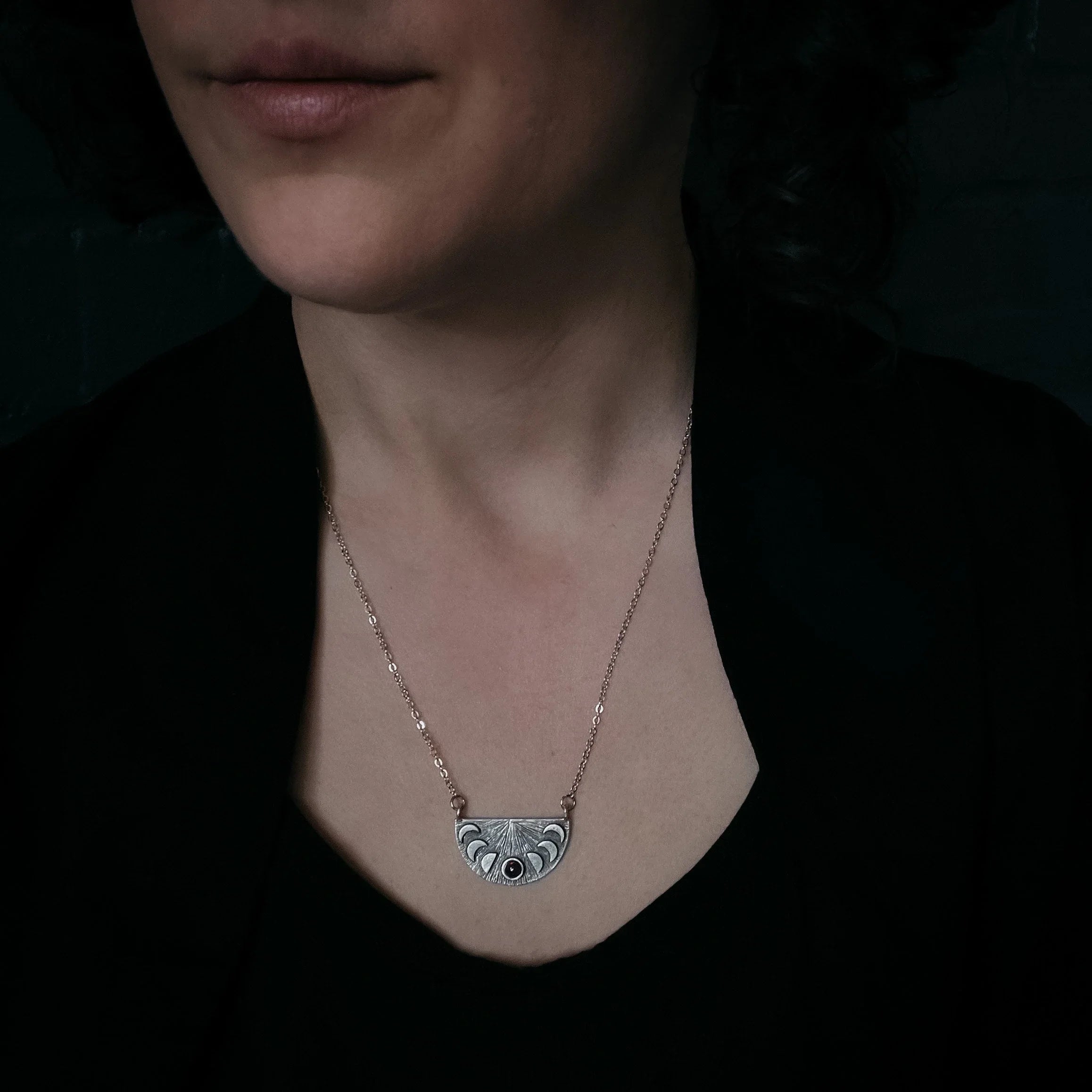 Person wearing a silver necklace with a half-circle pendant featuring engraved shapes and a black stone