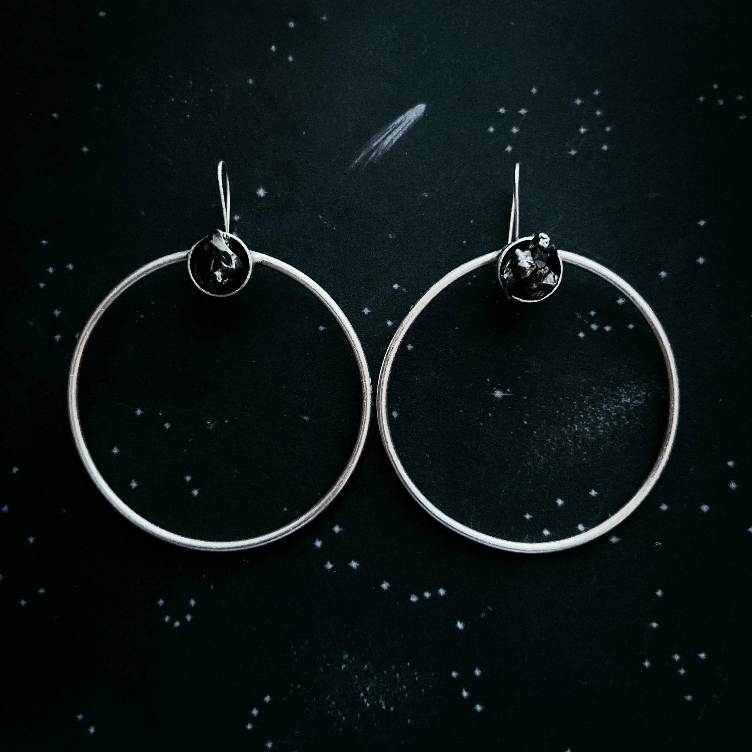 Silver hoop earrings with black stone accents on dark starry night background
