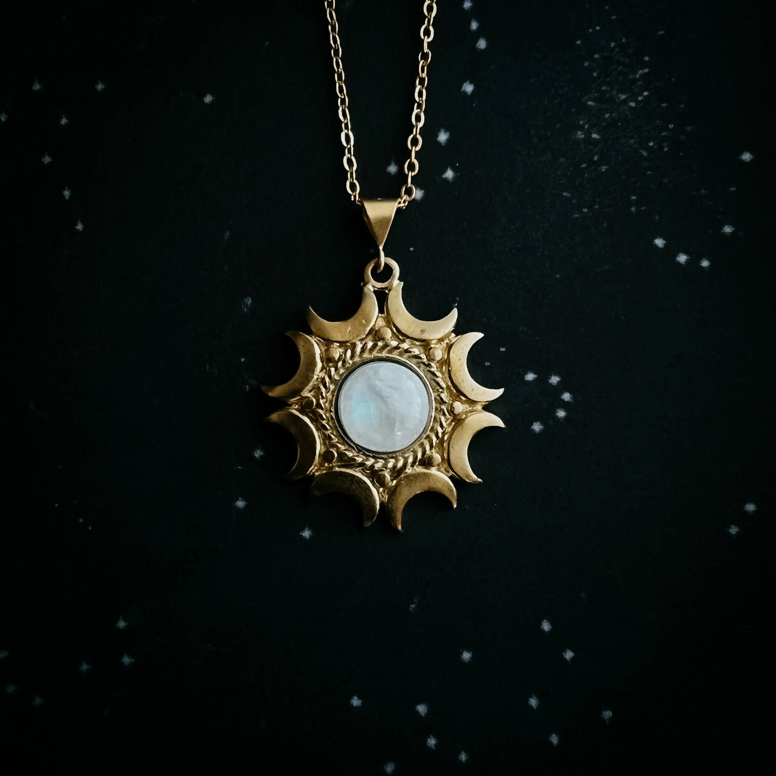 Gold sun-shaped pendant with crescent moon details and a round white center stone on a gold chain