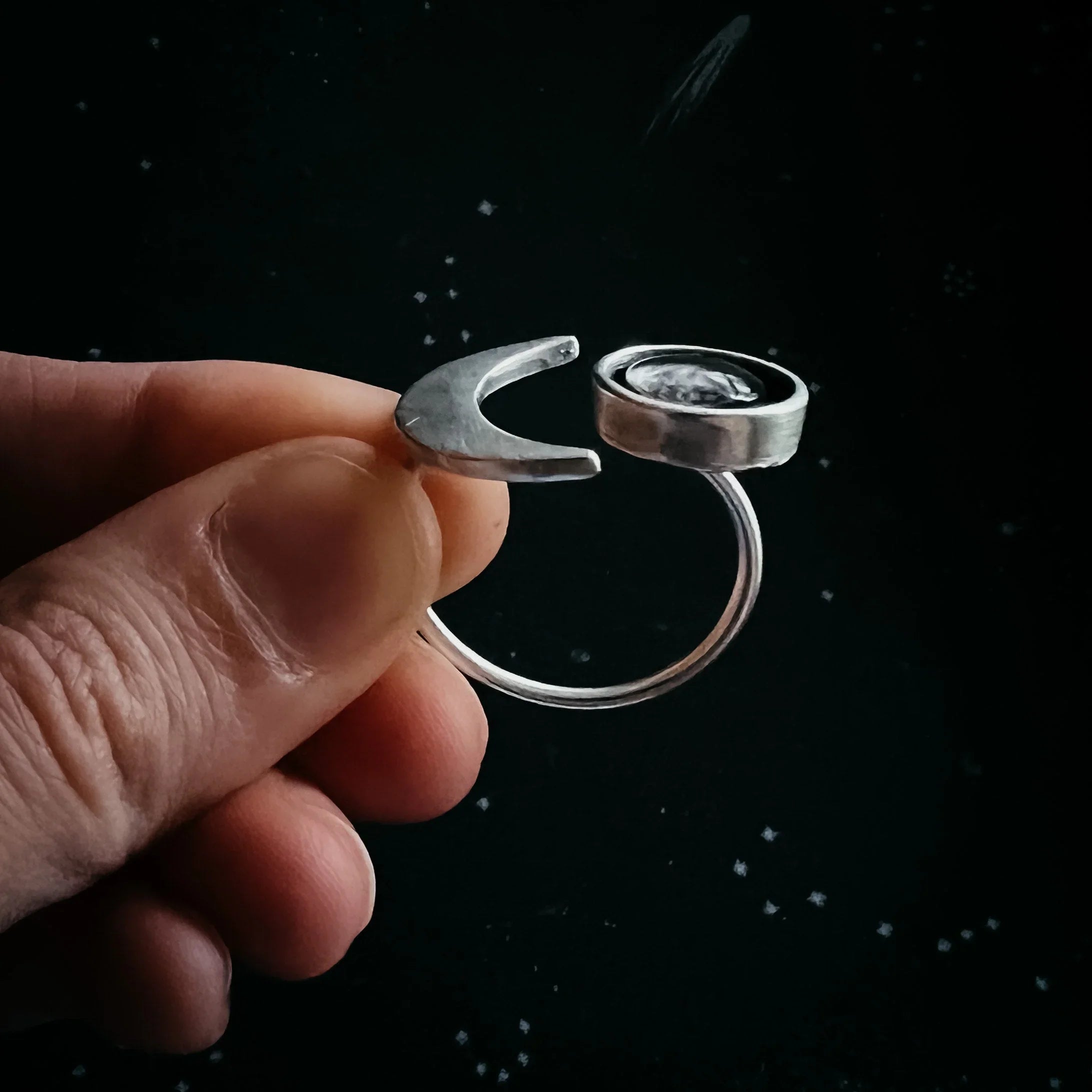 Hand holding silver open ring with crescent moon and round bezel holding a clear stone