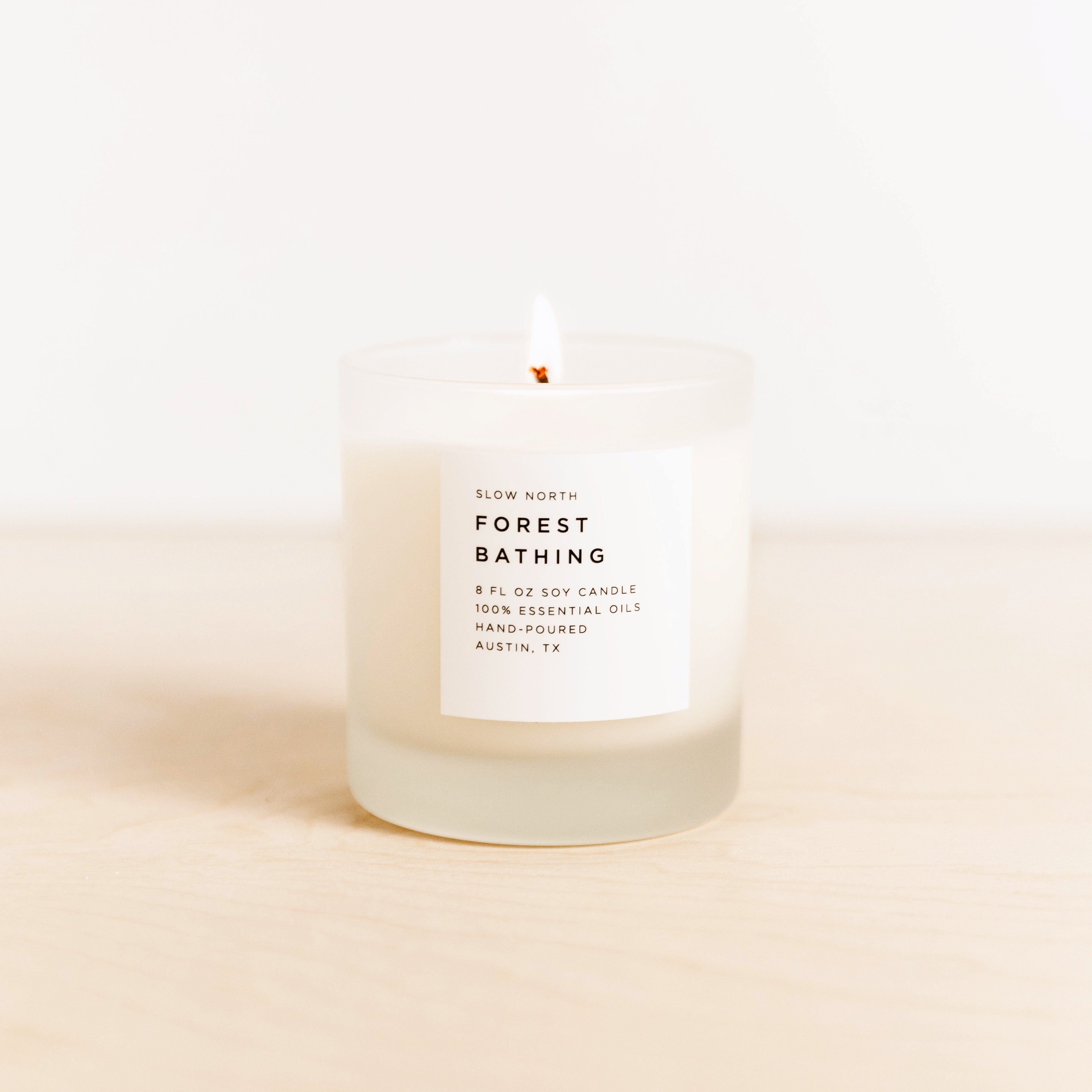 Lit Slow North Forest Bathing scented soy candle in frosted glass on wooden surface