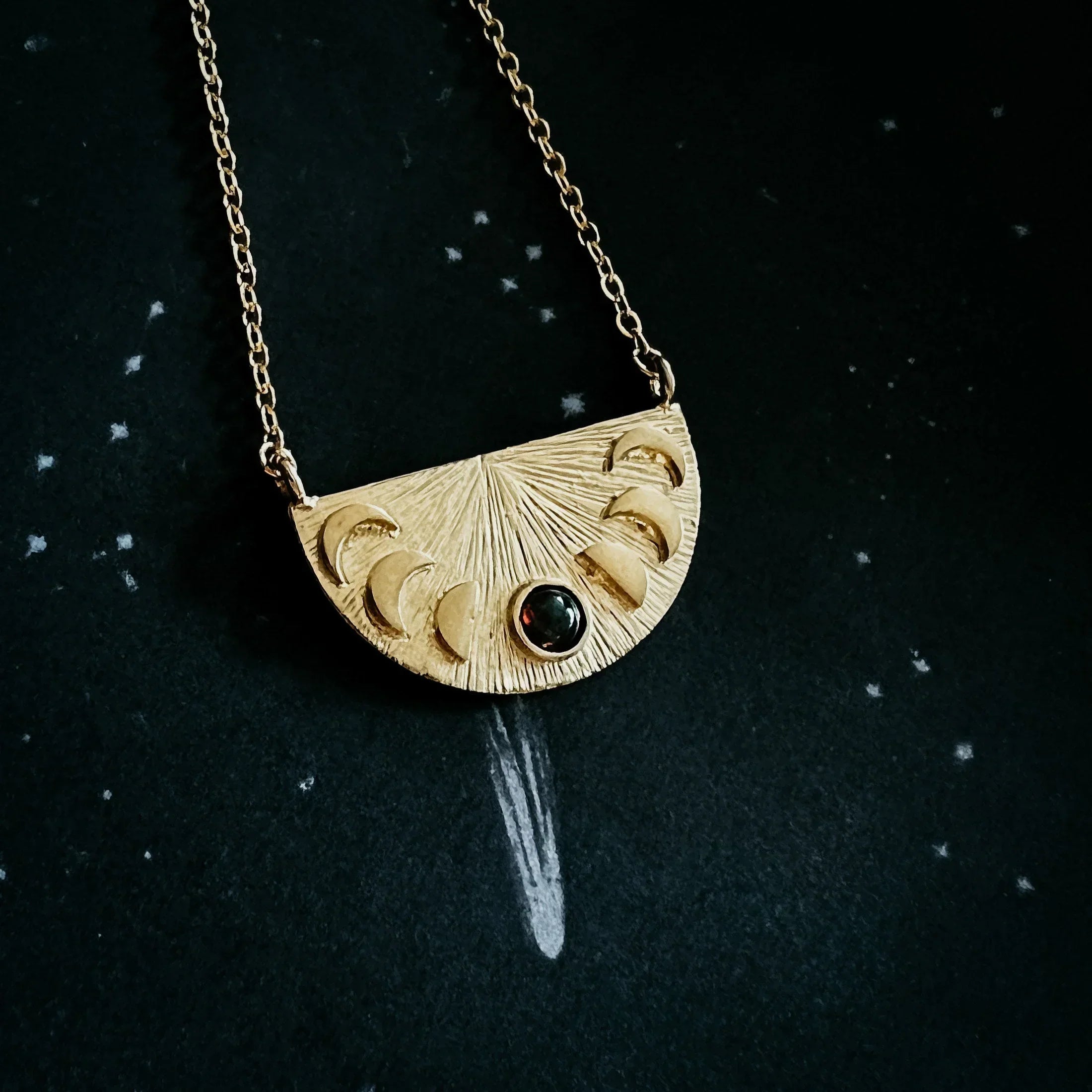 Gold crescent moon phase pendant necklace with black stone on dark starry background