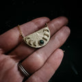Hand holding gold crescent moon phase necklace pendant with green gemstone on dark background