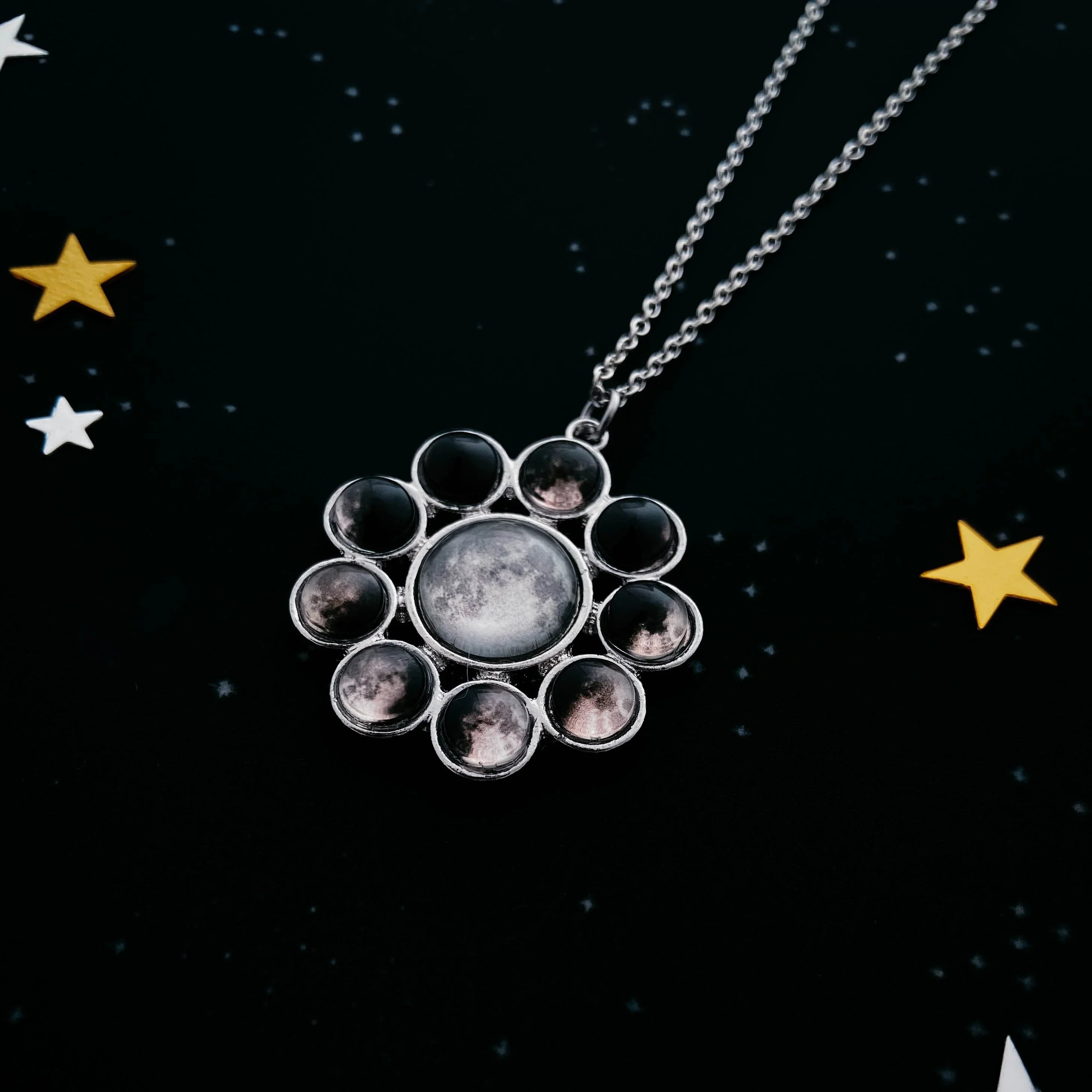 Silver moon phase pendant necklace on a starry black background with gold and white star accents