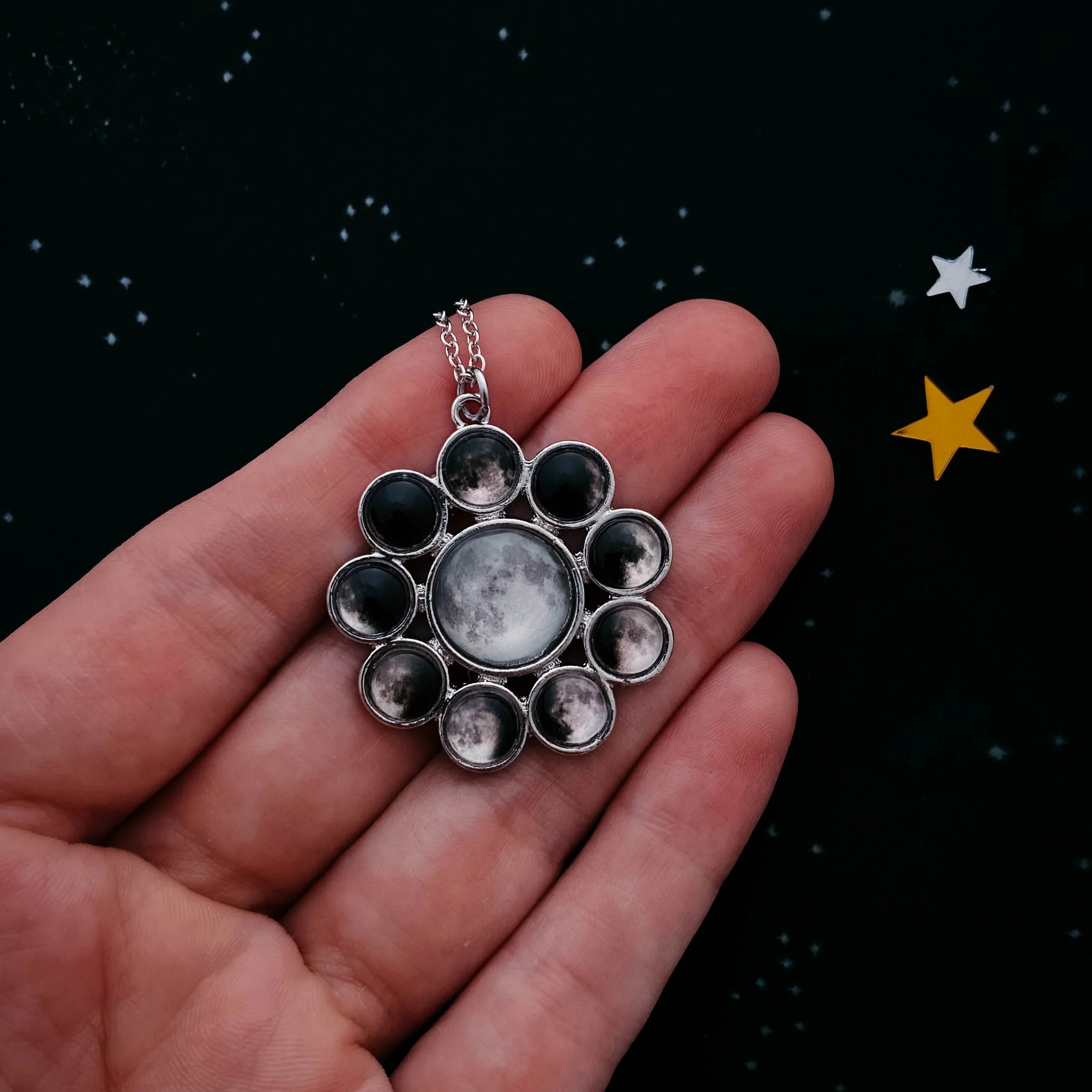 Hand holding a cosmic lunar phase necklace on black starry background, Qu!rk Boutique