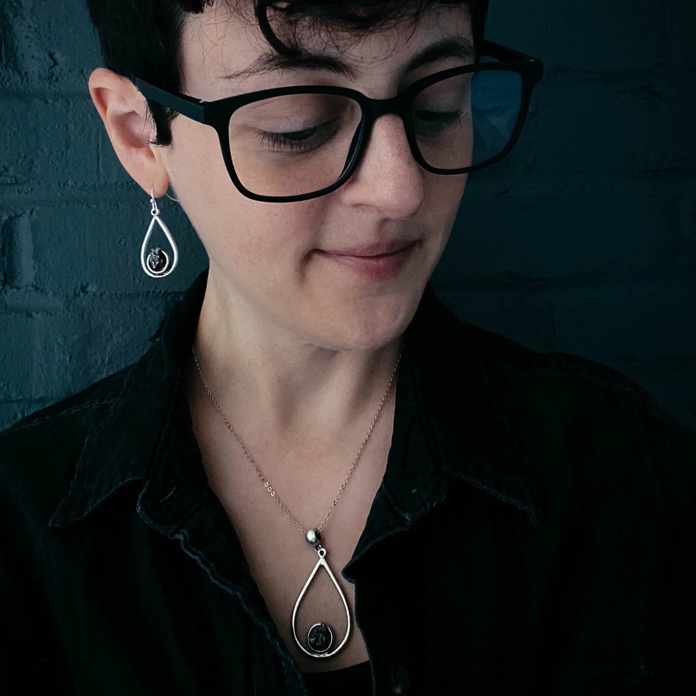 Woman wearing black glasses and black shirt with matching silver teardrop earrings and necklace