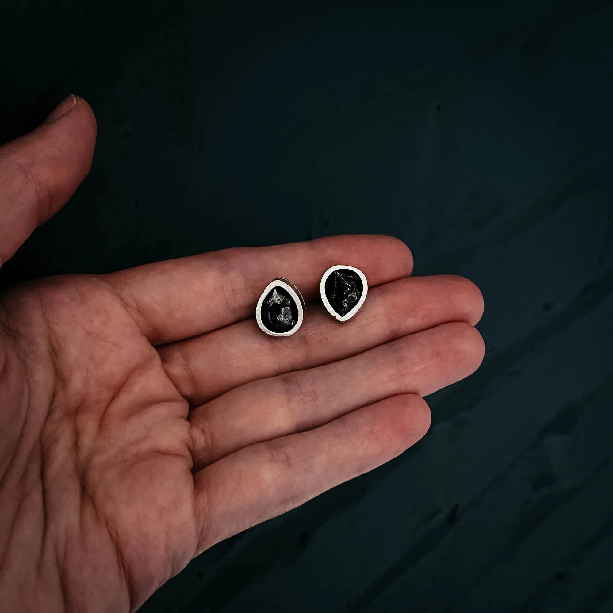 Hand holding teardrop-shaped black gemstone stud earrings, artist-designed jewelry